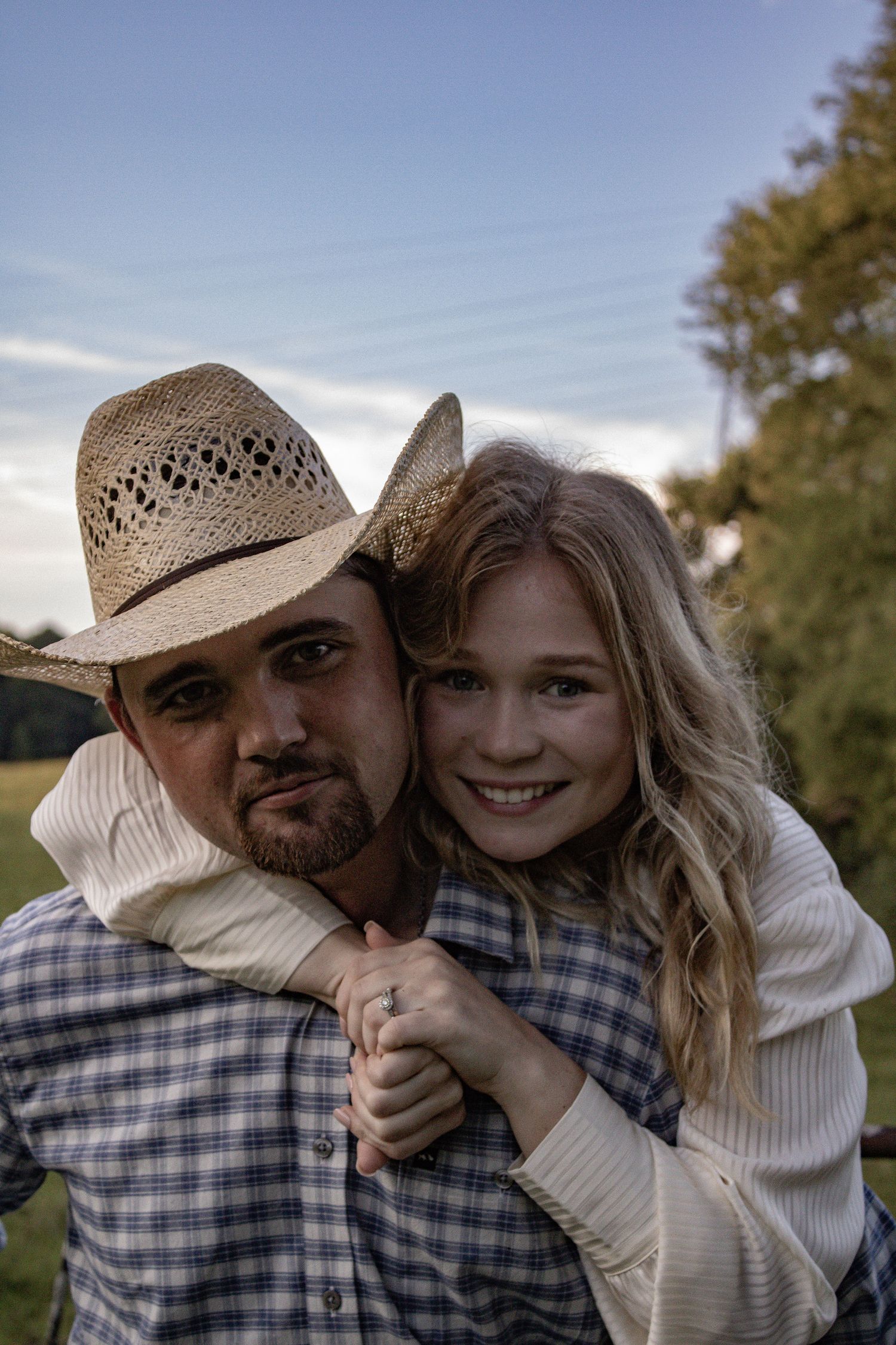 Couple in casual attire and cowboy hat sharing intimate moments outdoors.