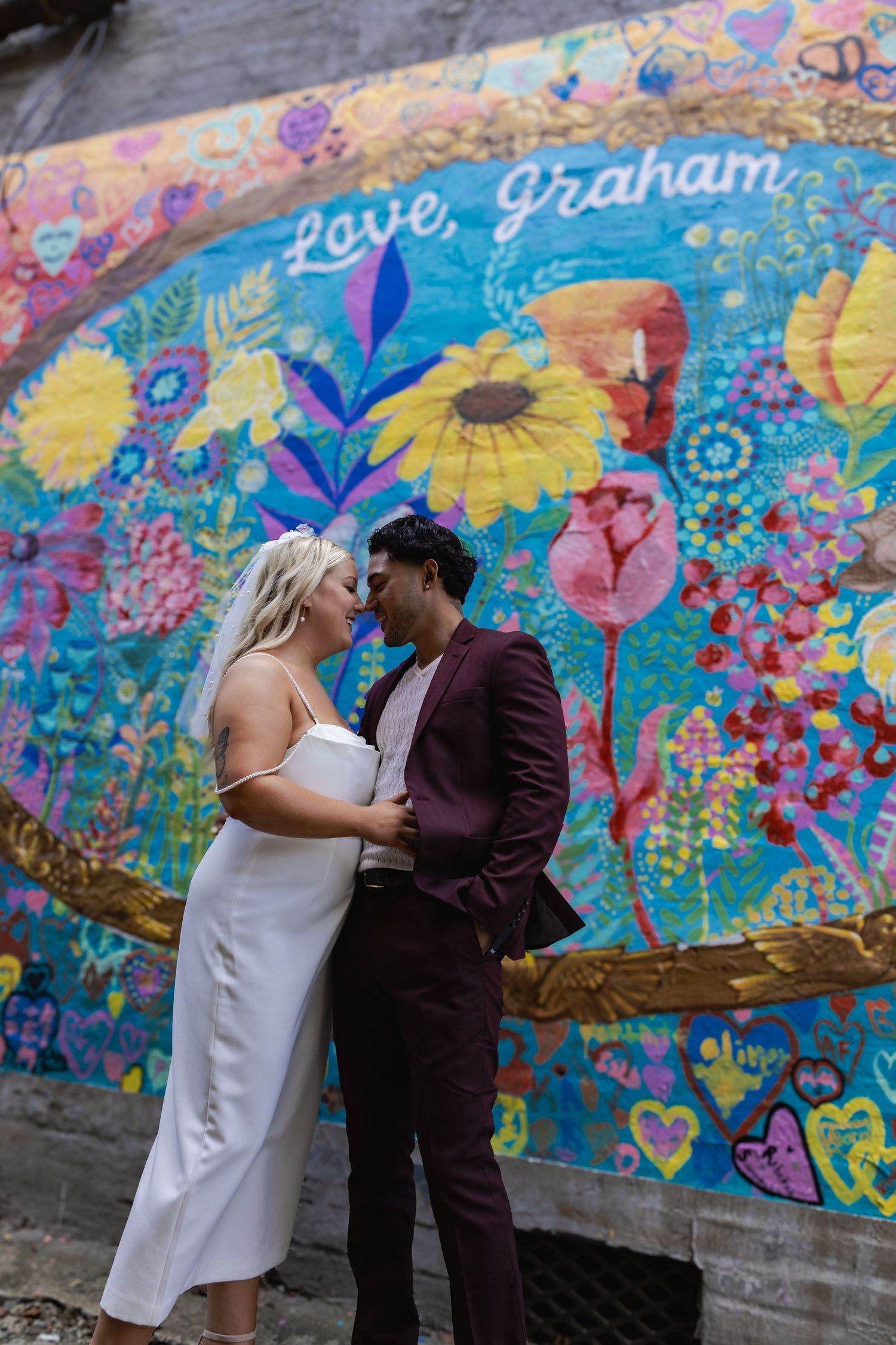 A romantic couple pose in front of a whimsical garden mural with bright flowers.