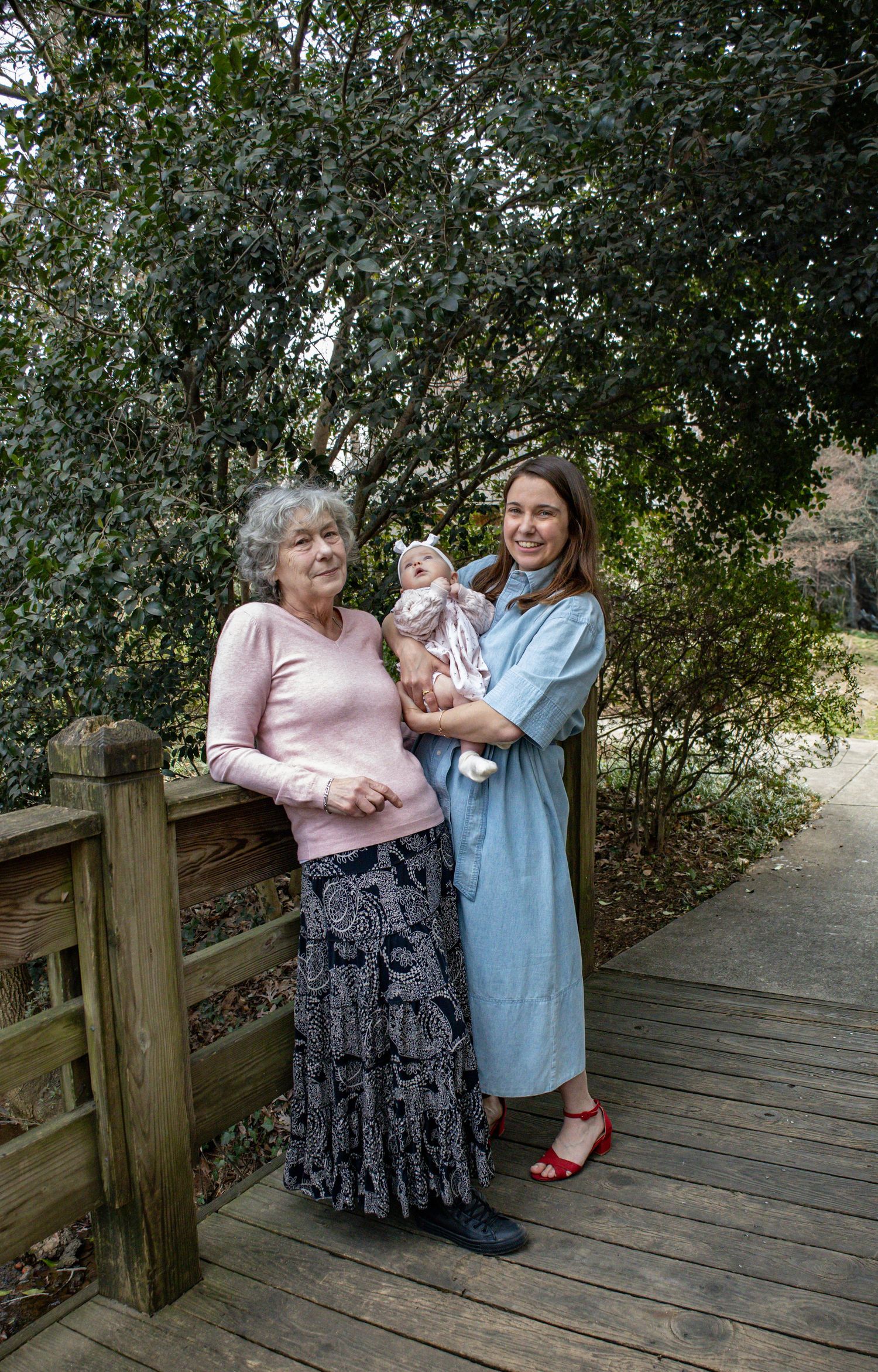 Three generations pose together on a wooden boardwalk surrounded by green foliage.