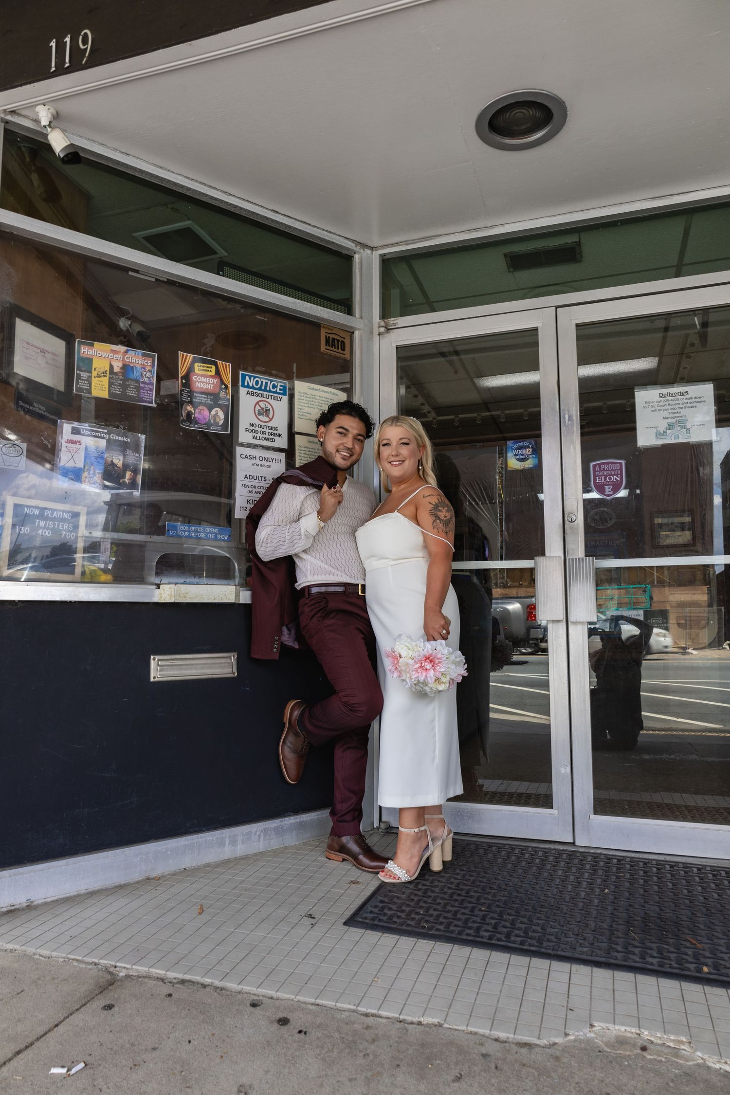 A couple poses in formal attire at the entrance of a small business storefront.