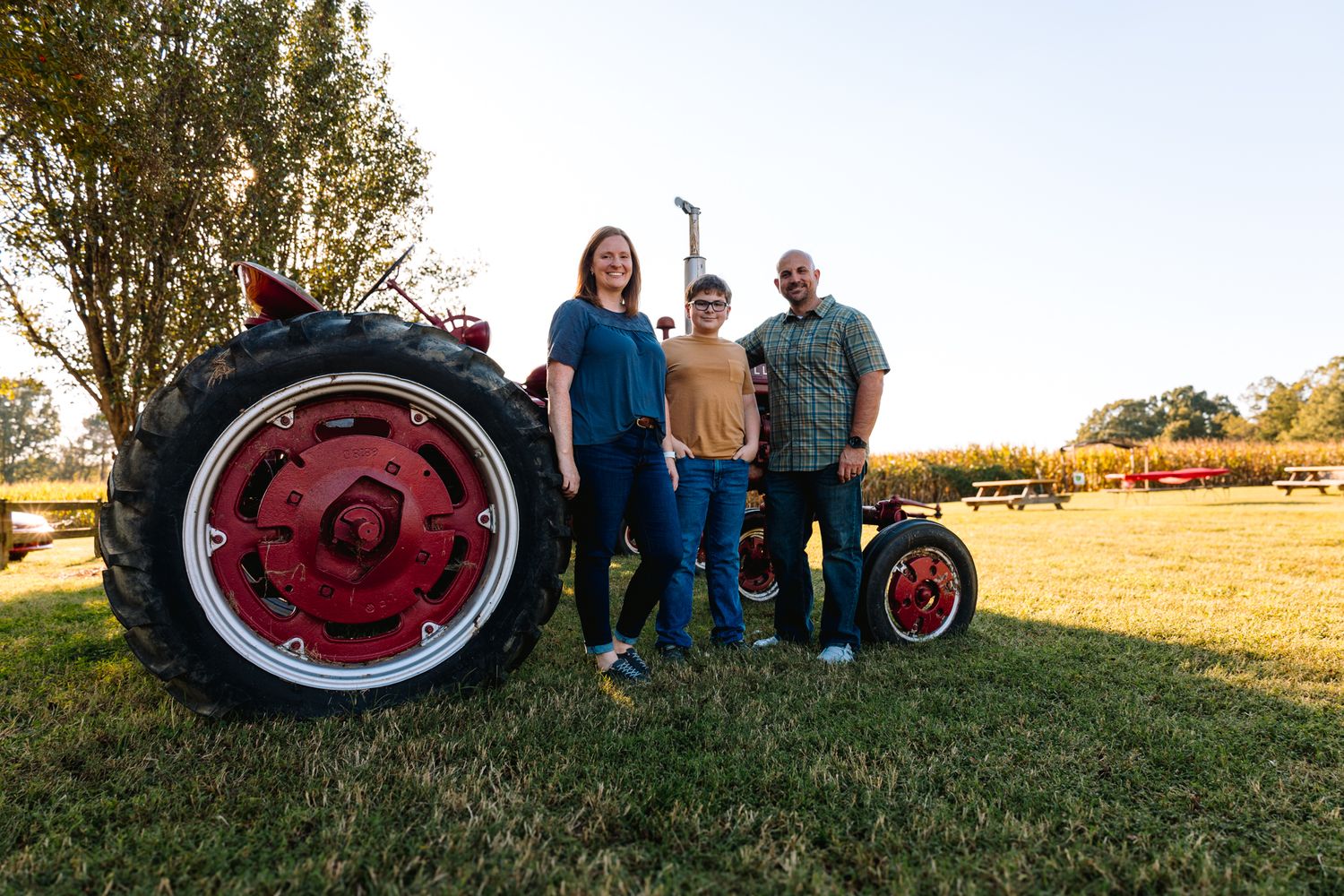 A group poses with a vintage red tractor in a golden field at sunset.