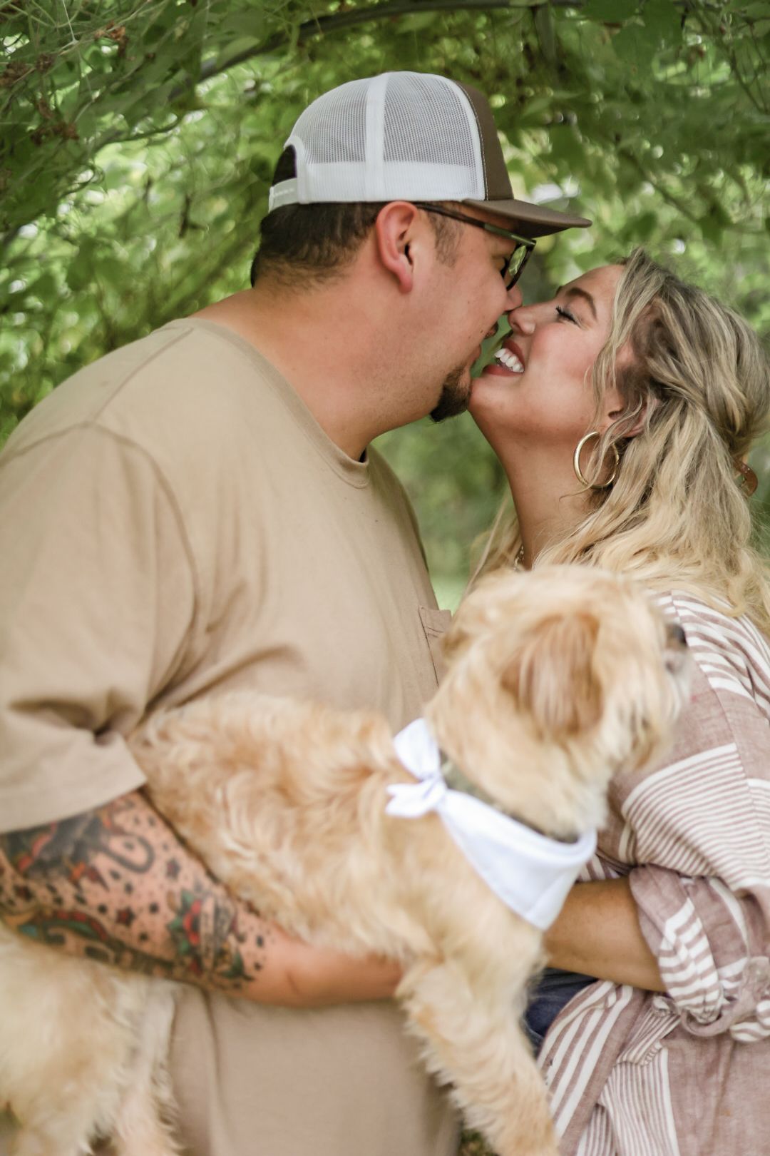 Couple shares intimate moment with their golden retriever in lush outdoor setting.