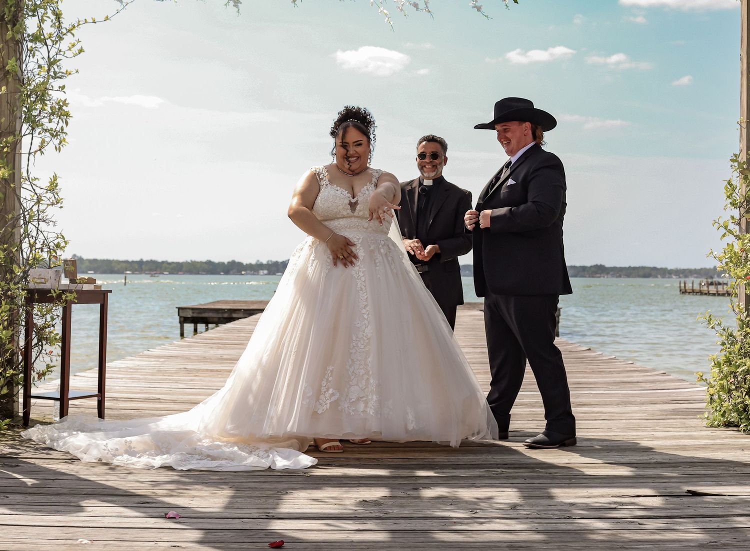 Wedding couple dancing on a waterfront deck under floral archway.