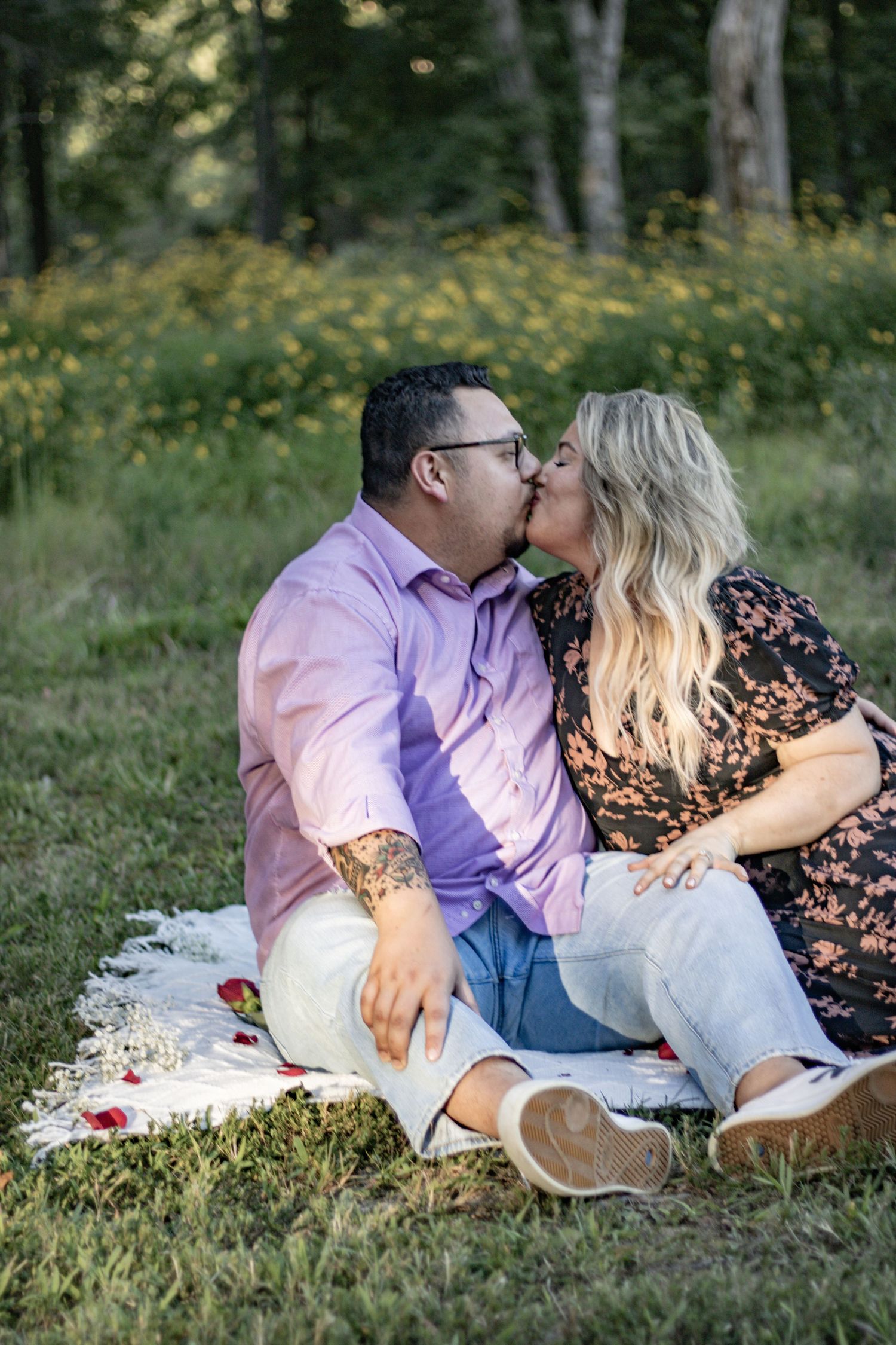 A couple shares an intimate kiss during a romantic picnic on a blanket in a meadow.