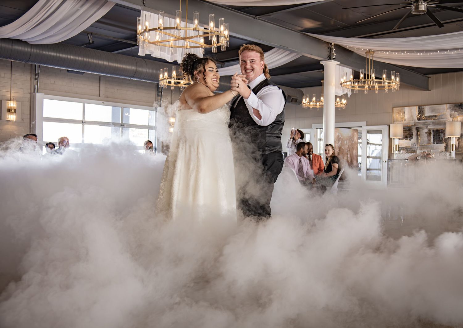 A couple shares their first dance surrounded by atmospheric fog on an elegant reception dance floor.