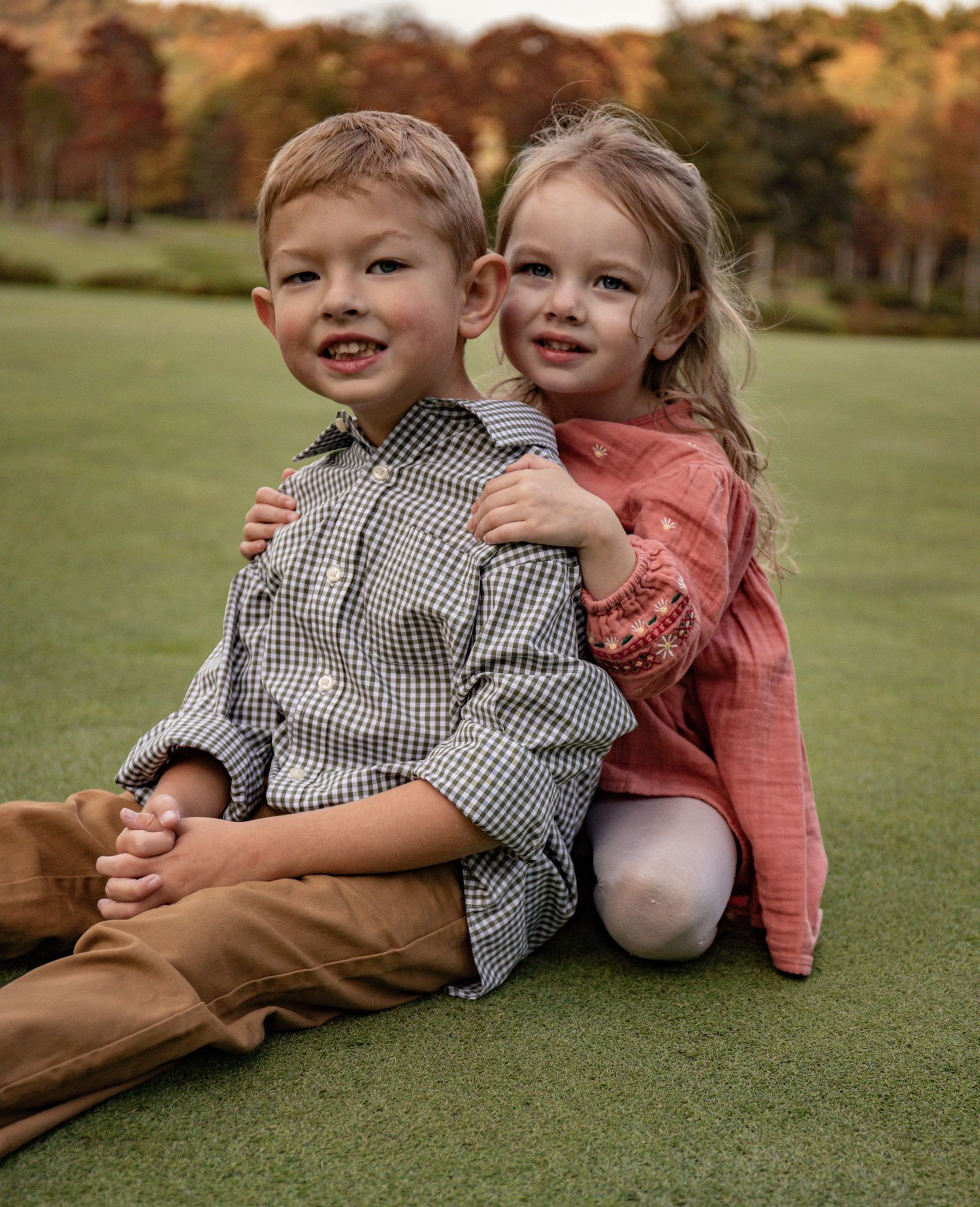 Two children laying on grass in autumn wearing coordinated outfits in warm earth tones.
