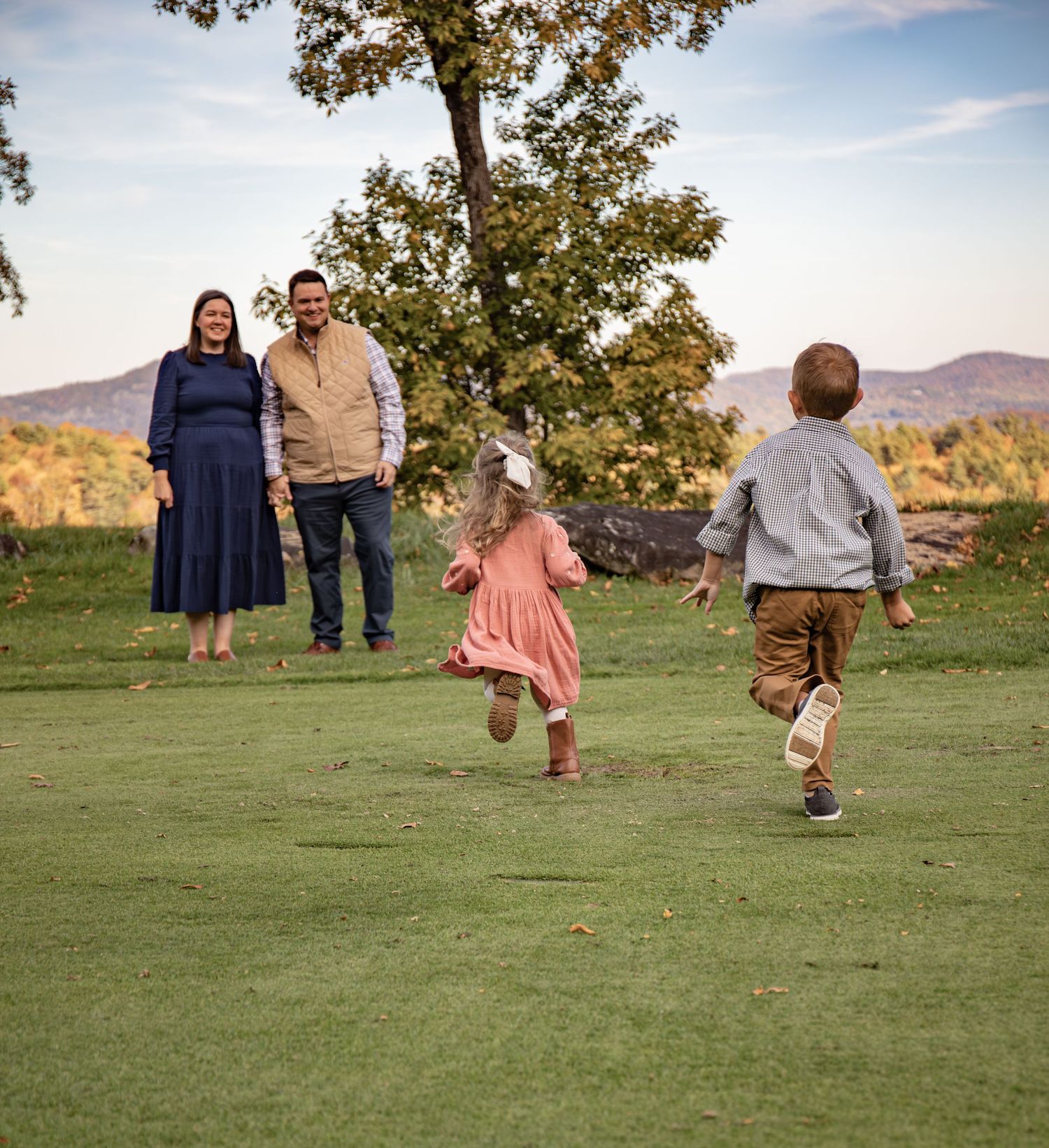 Family members run and play together on a grassy hillside during a golden autumn afternoon.