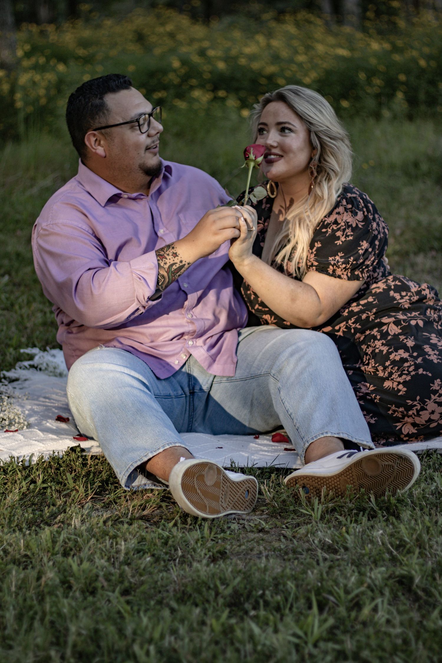 A couple shares a romantic moment with a red rose while sitting on a picnic blanket.