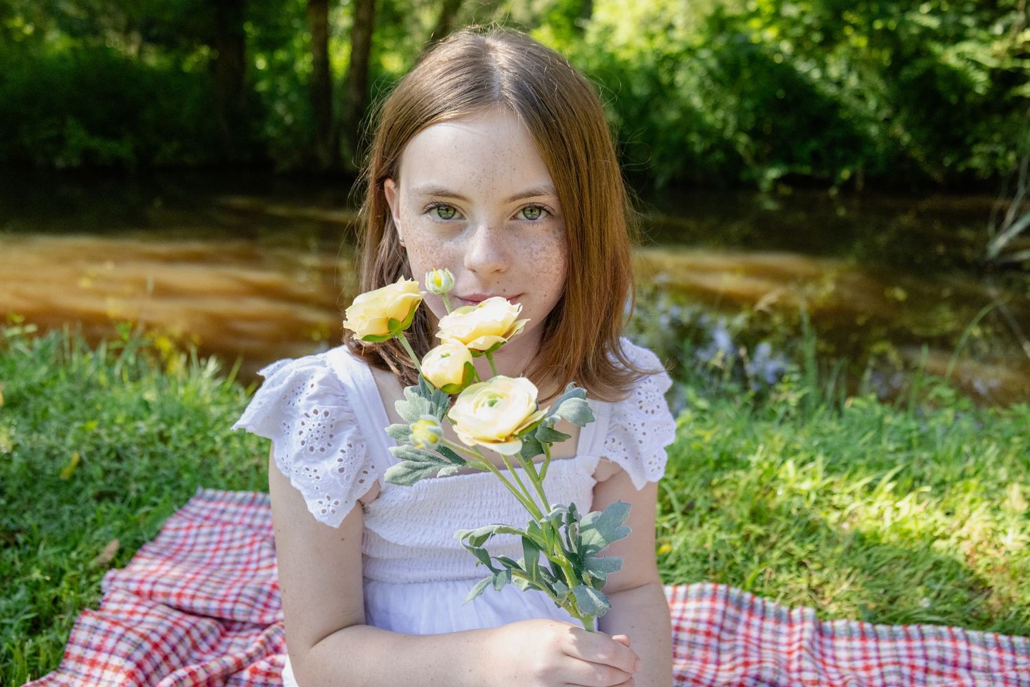 A white dress-clad figure enjoys a picnic on a red checkered blanket in a sunlit forest setting.