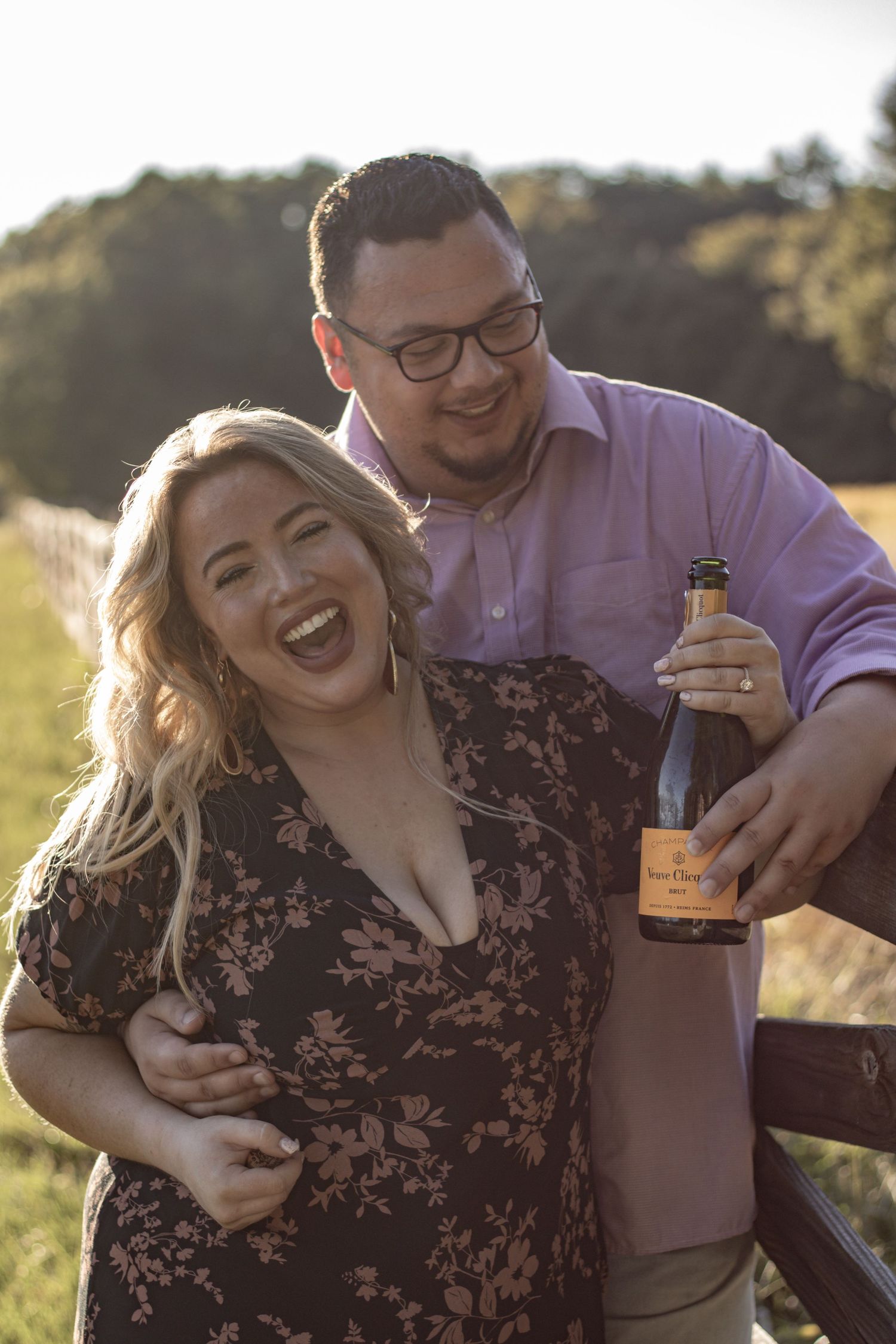 Joyful couple sharing intimate moment outdoors with champagne bottle at sunset.