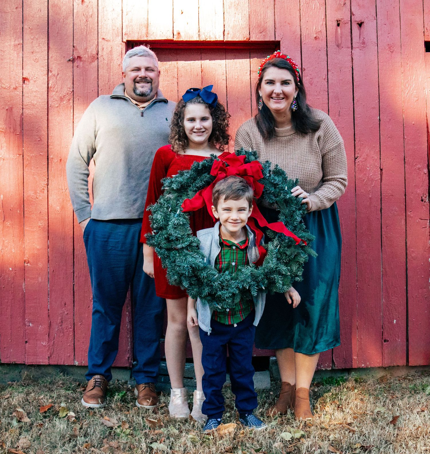 Holiday portrait session with evergreen wreath against rustic red barn backdrop.