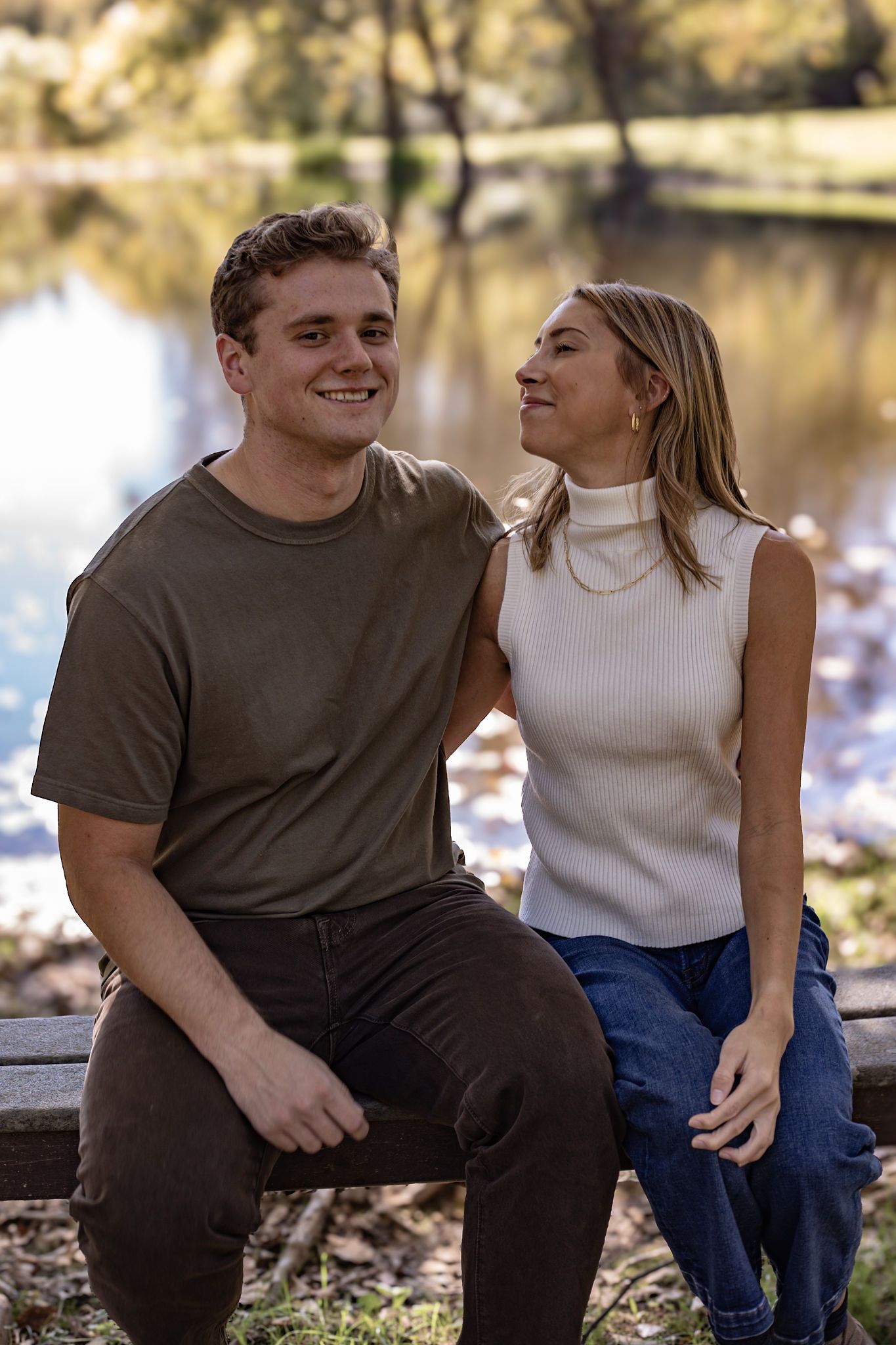 A romantic couple sharing a joyful moment together while sitting by a lake on a sunny afternoon.
