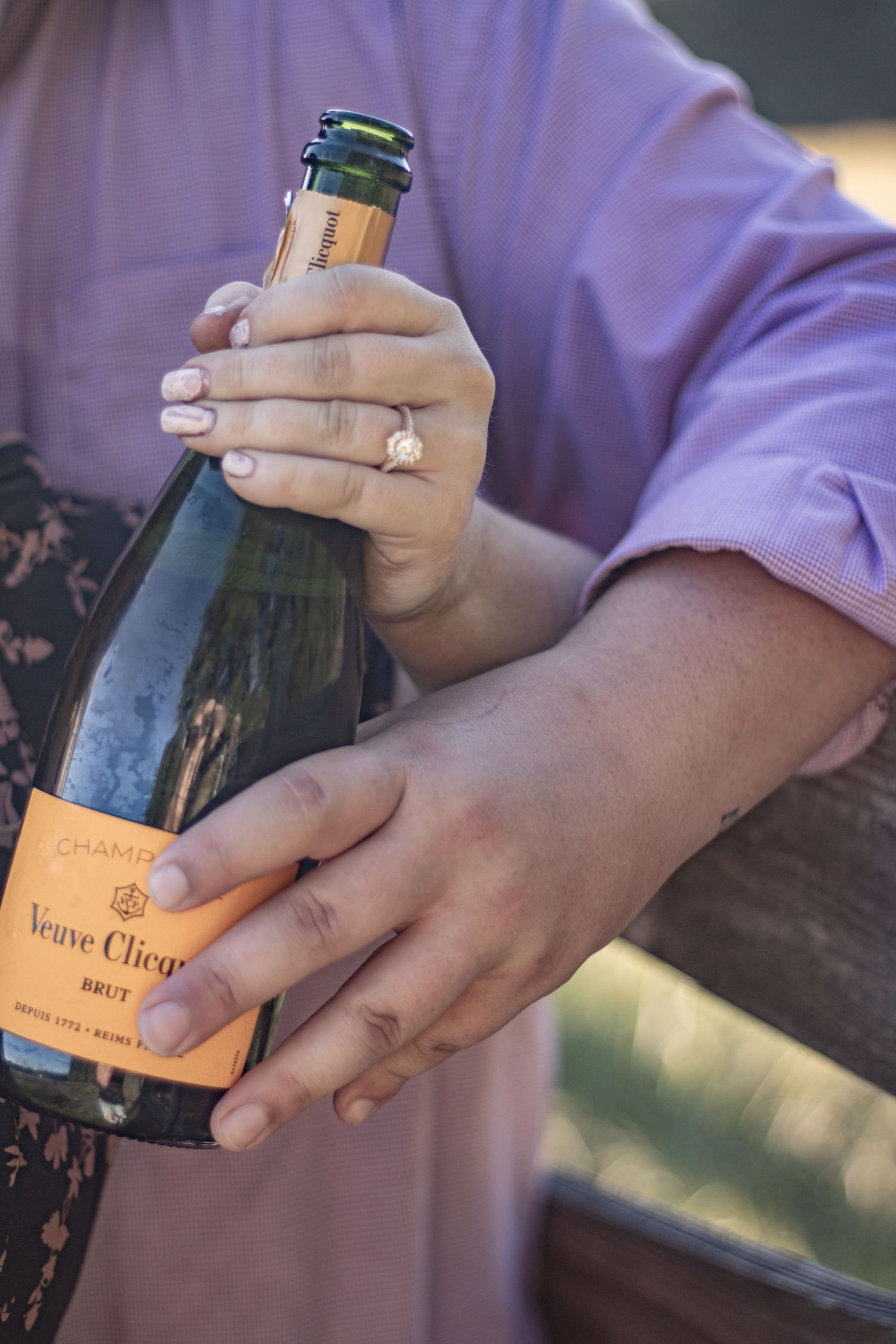 Hands hold a bottle of Veuve Clicquot champagne showing a sparkling engagement ring.