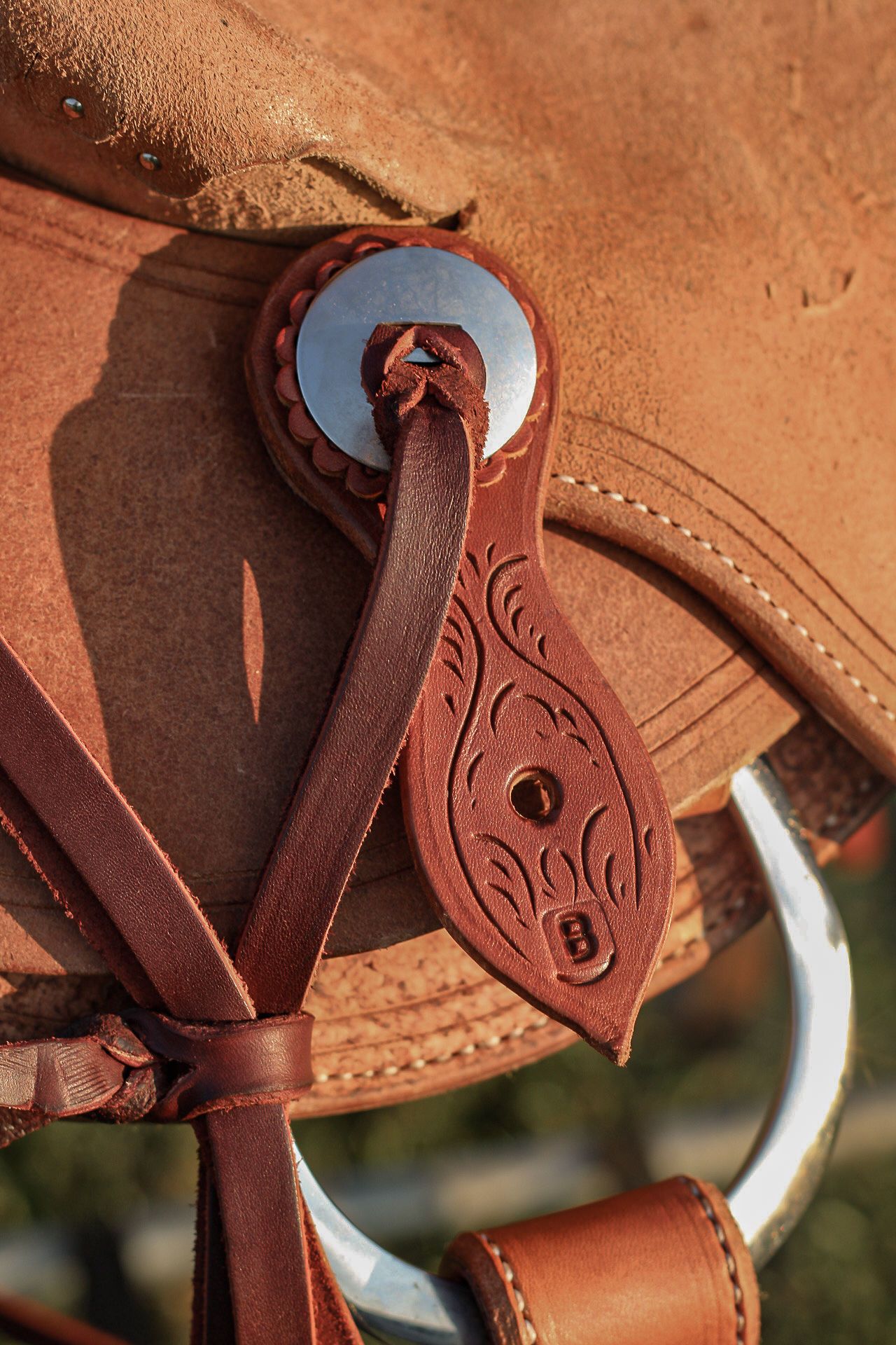 Close-up detail of a brown leather saddle showing decorative metal conchos and tooled leather patterns.