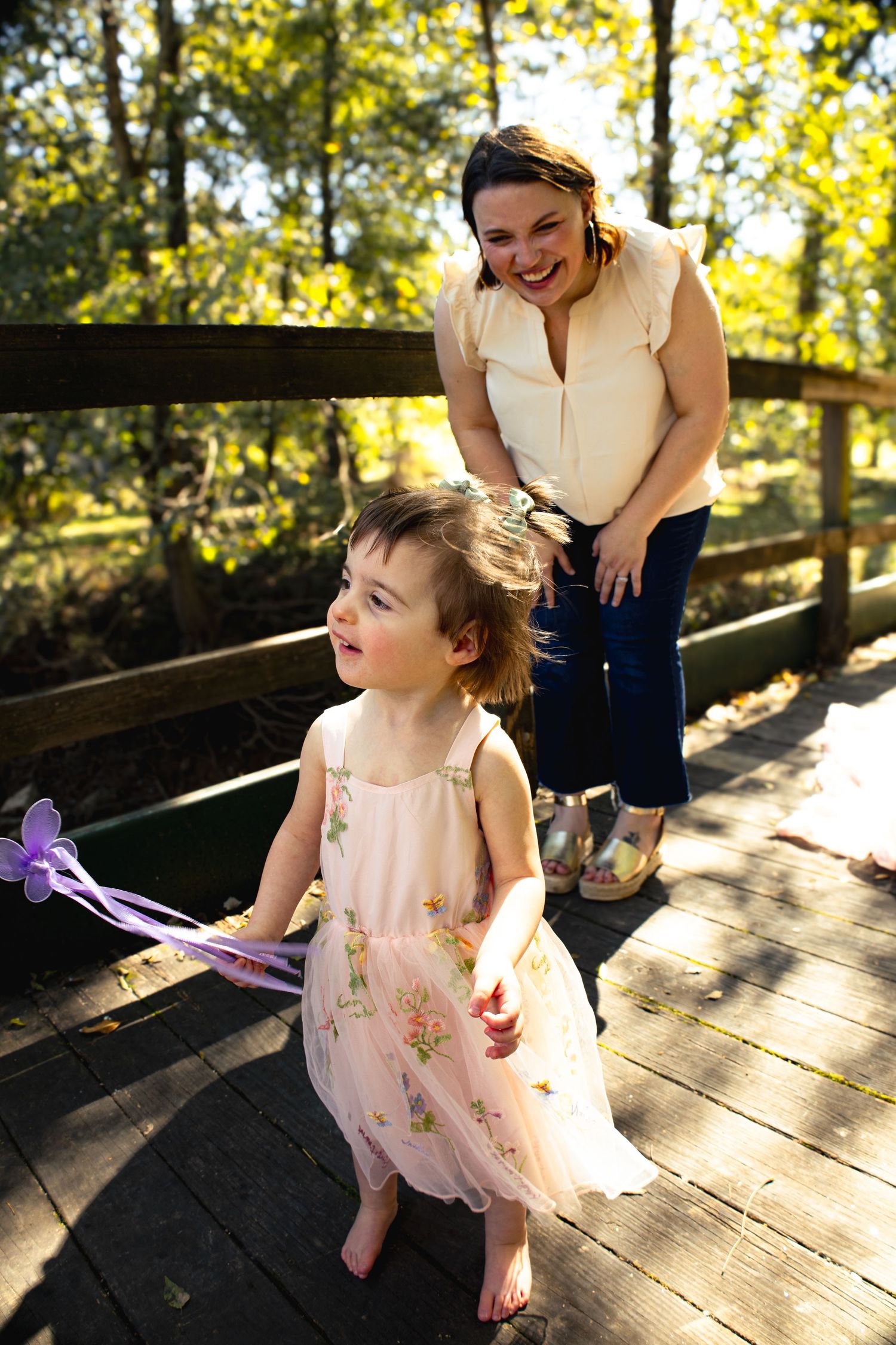 A delicate pink dress twirls on a wooden bridge while sunlight filters through the trees.