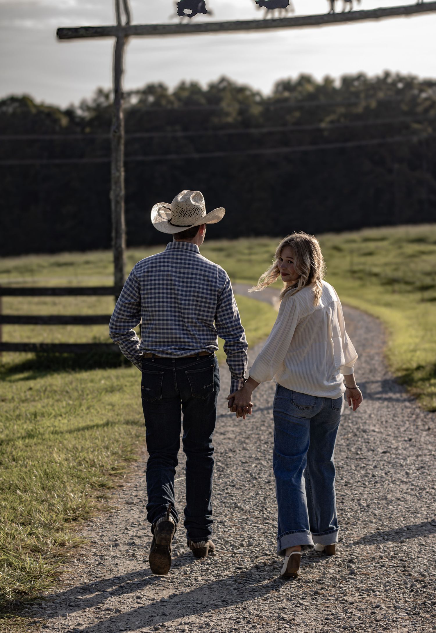 A couple walking hand in hand down a country path, with one wearing a cowboy hat.