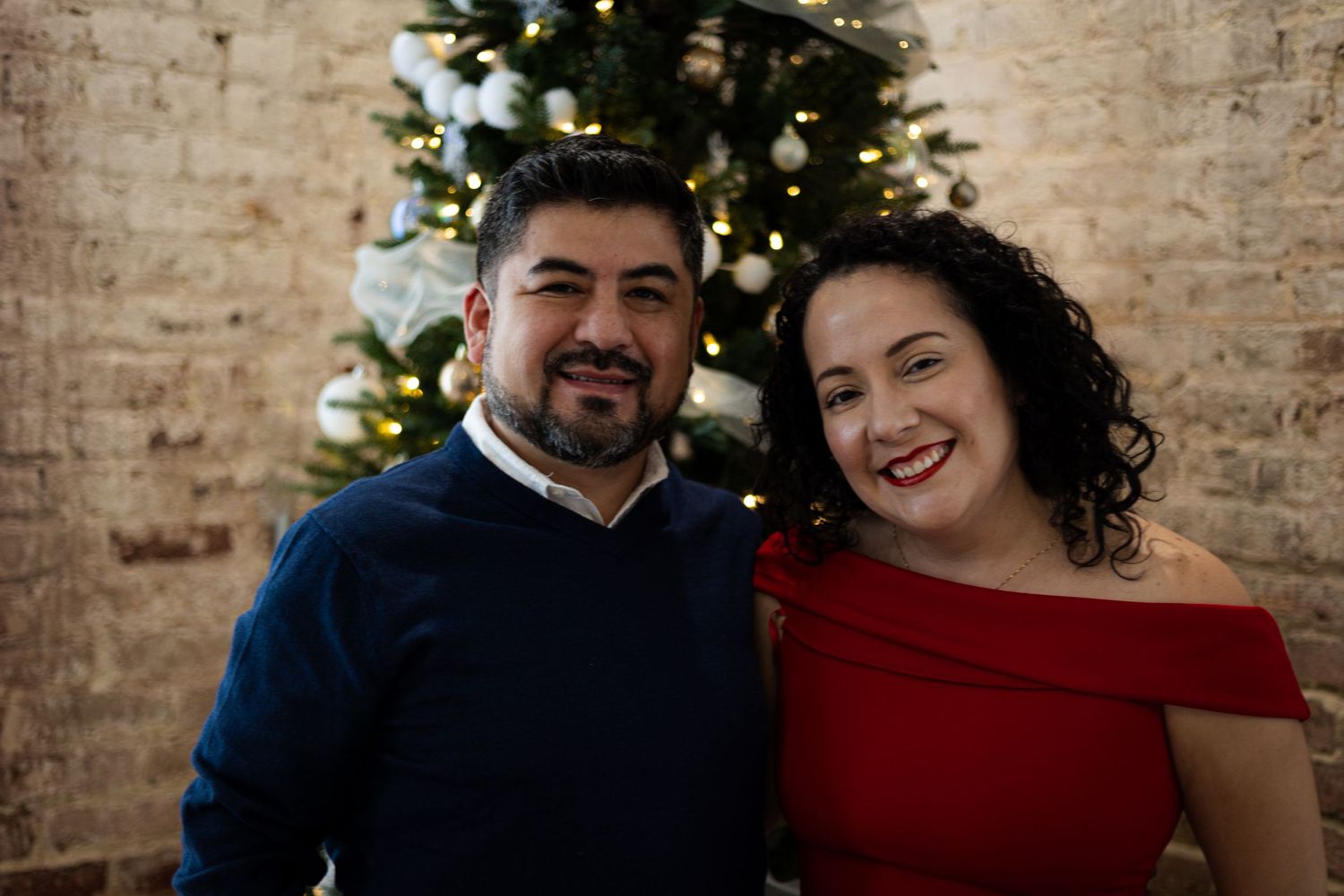 Holiday portrait of couple in navy and red attire in front of Christmas tree.