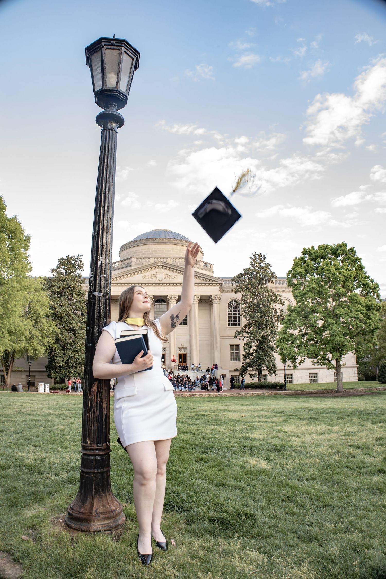 A graduate throws their cap in celebration near a lamp post on UNC campus.