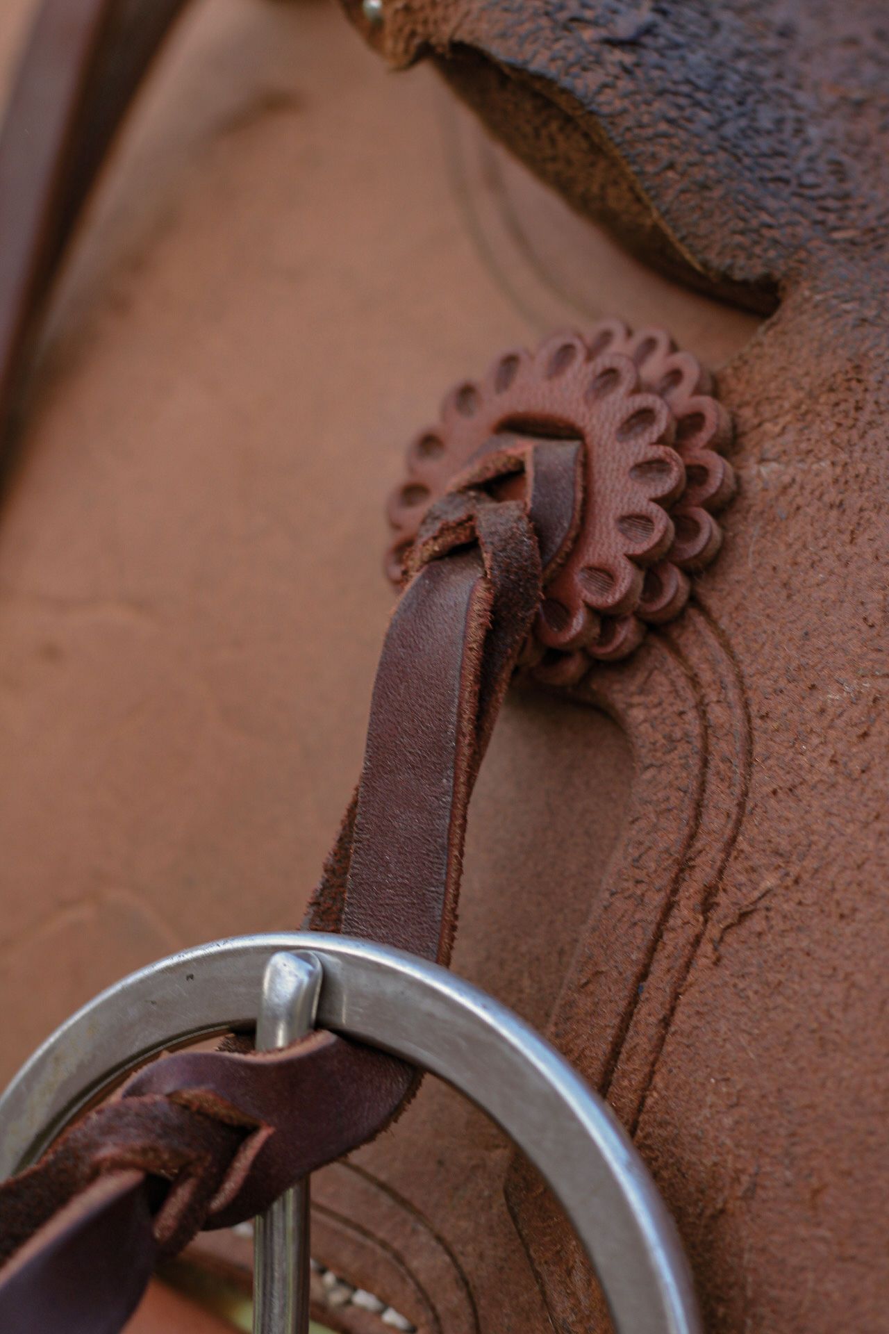 Close-up of ornate concho and leather strap detail on western saddle.