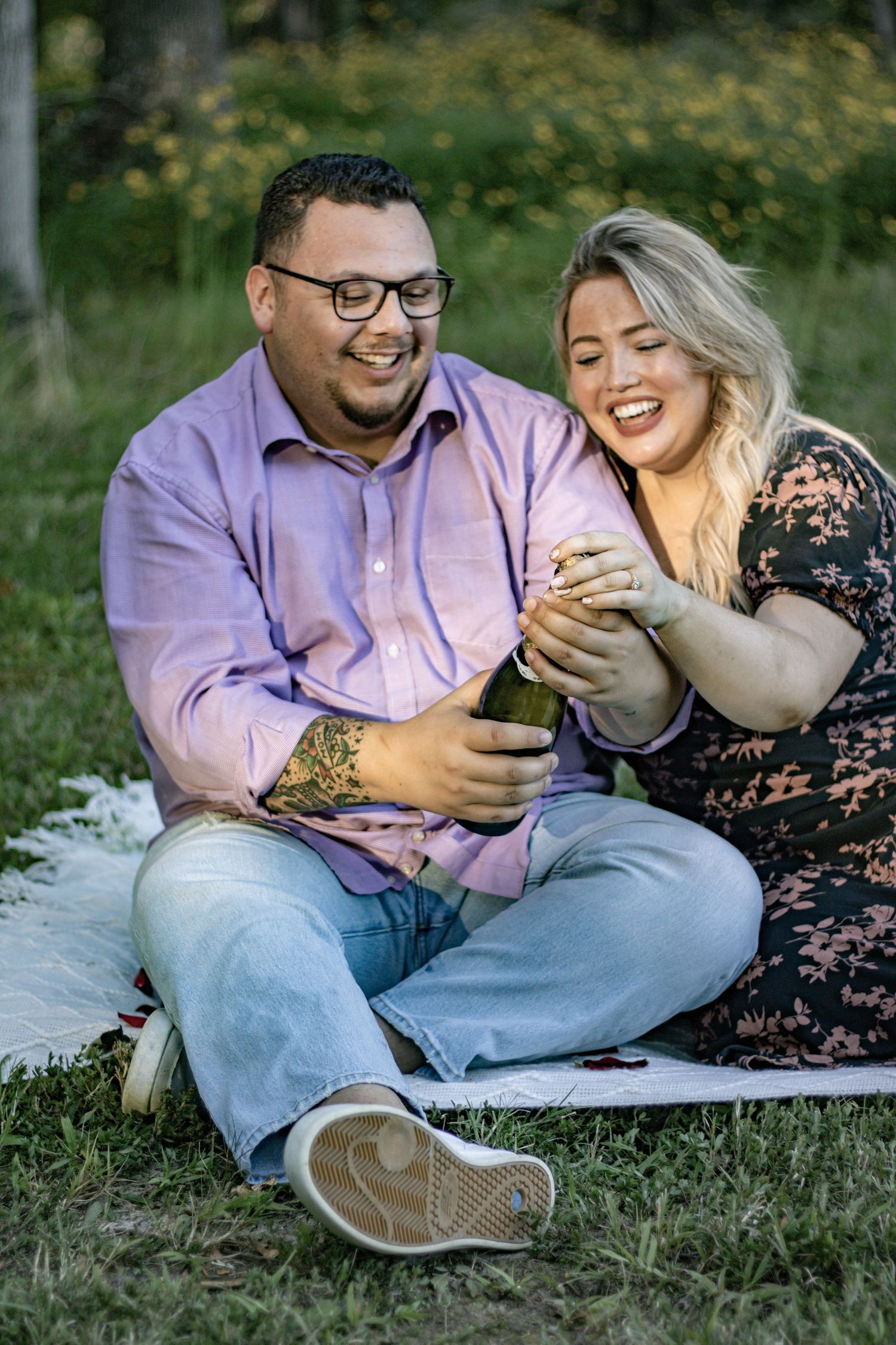 A couple shares joyful laughter while sitting together on a picnic blanket in a meadow.