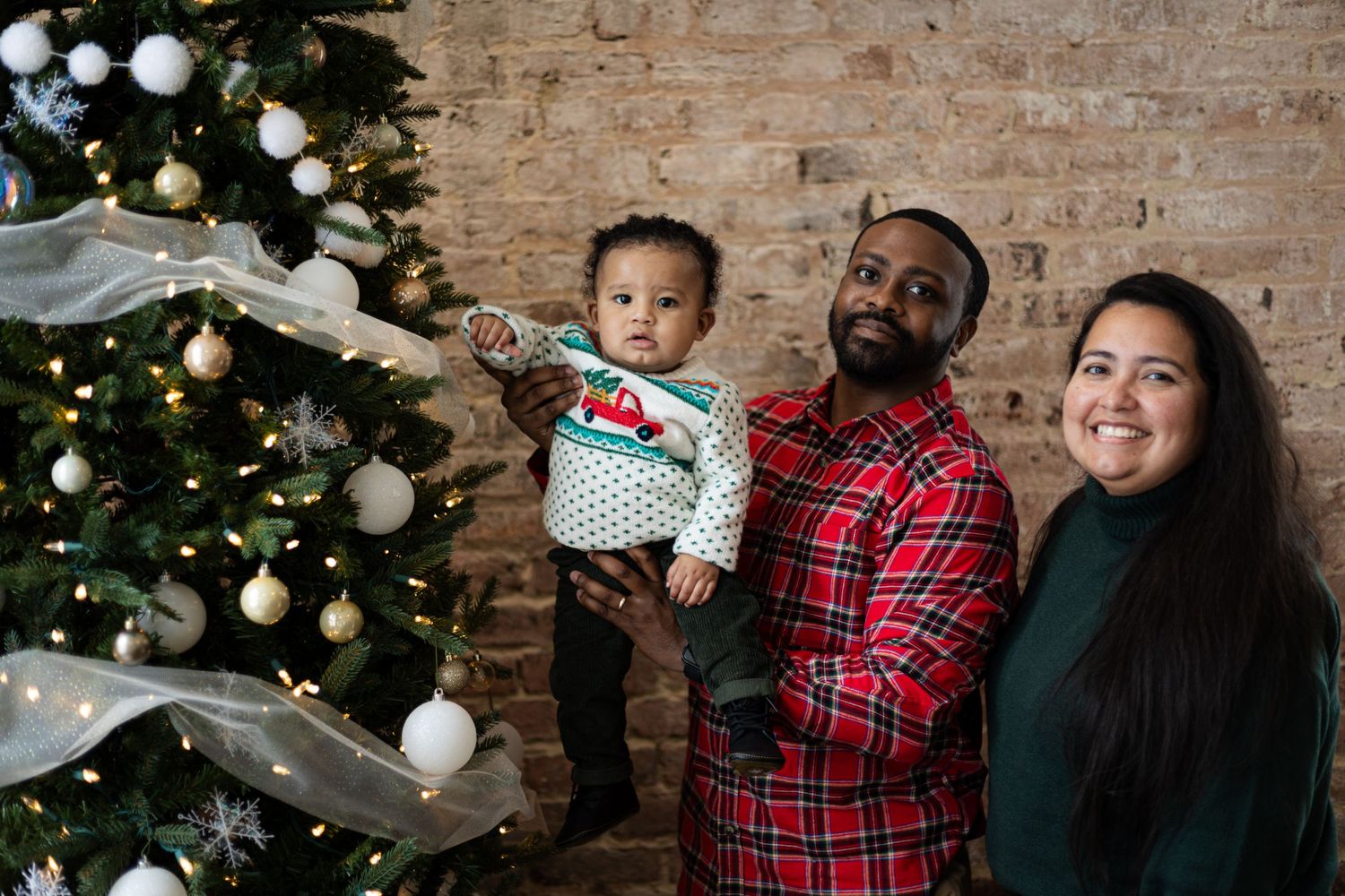 Family wearing red plaid and casual attire poses by Christmas tree with white ornaments.