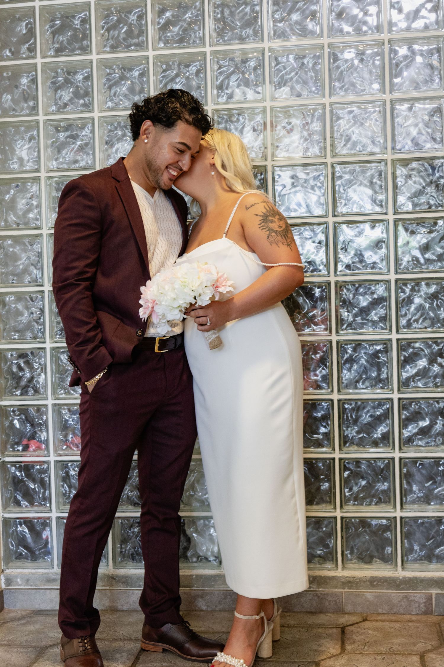 A romantic moment between a couple with white bouquet against a glass block backdrop.