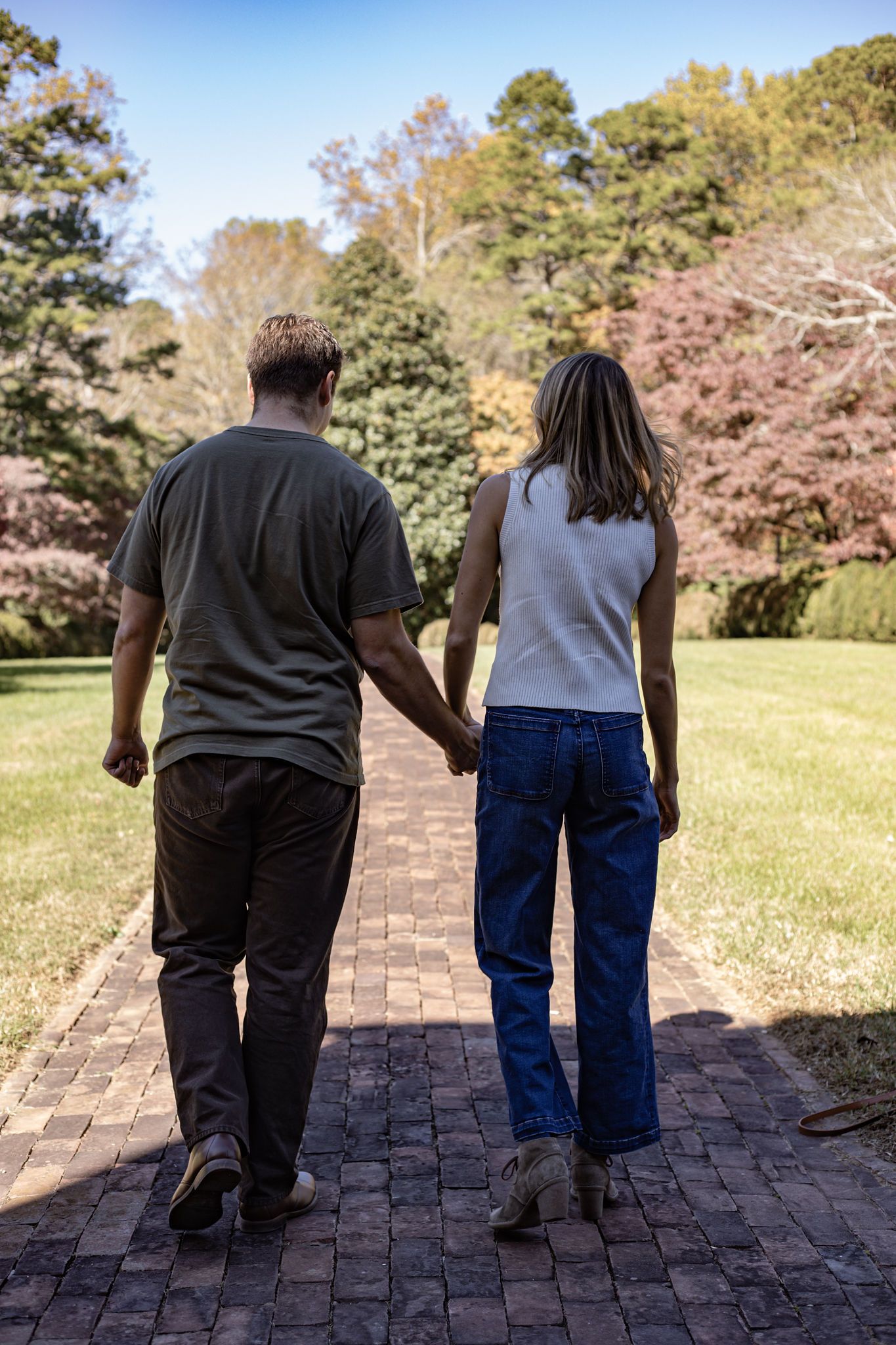 Couple walking hand in hand down a brick pathway surrounded by trees.