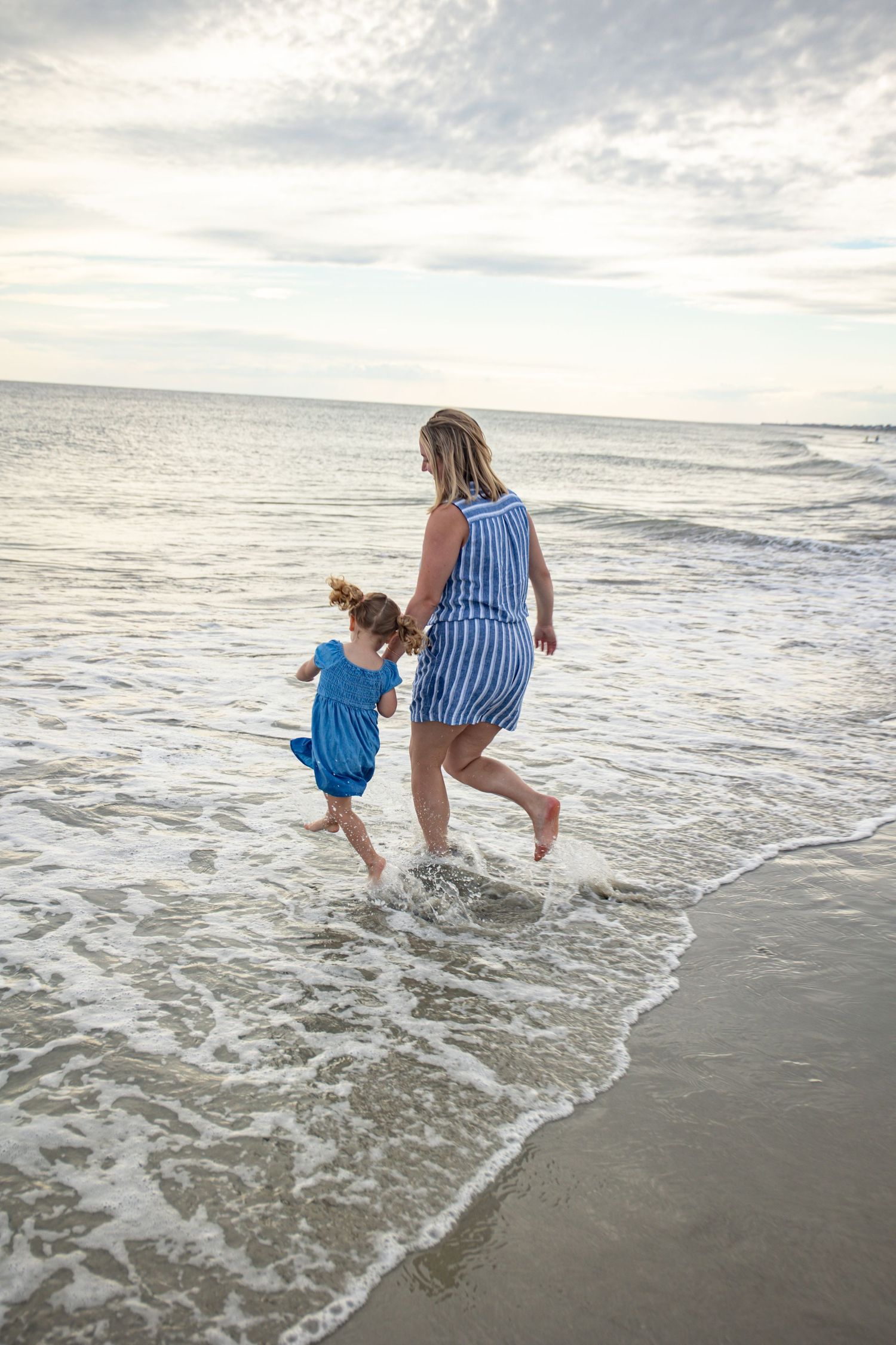 Two people in blue and white striped outfits playing together at the beach as waves roll in at sunset.
