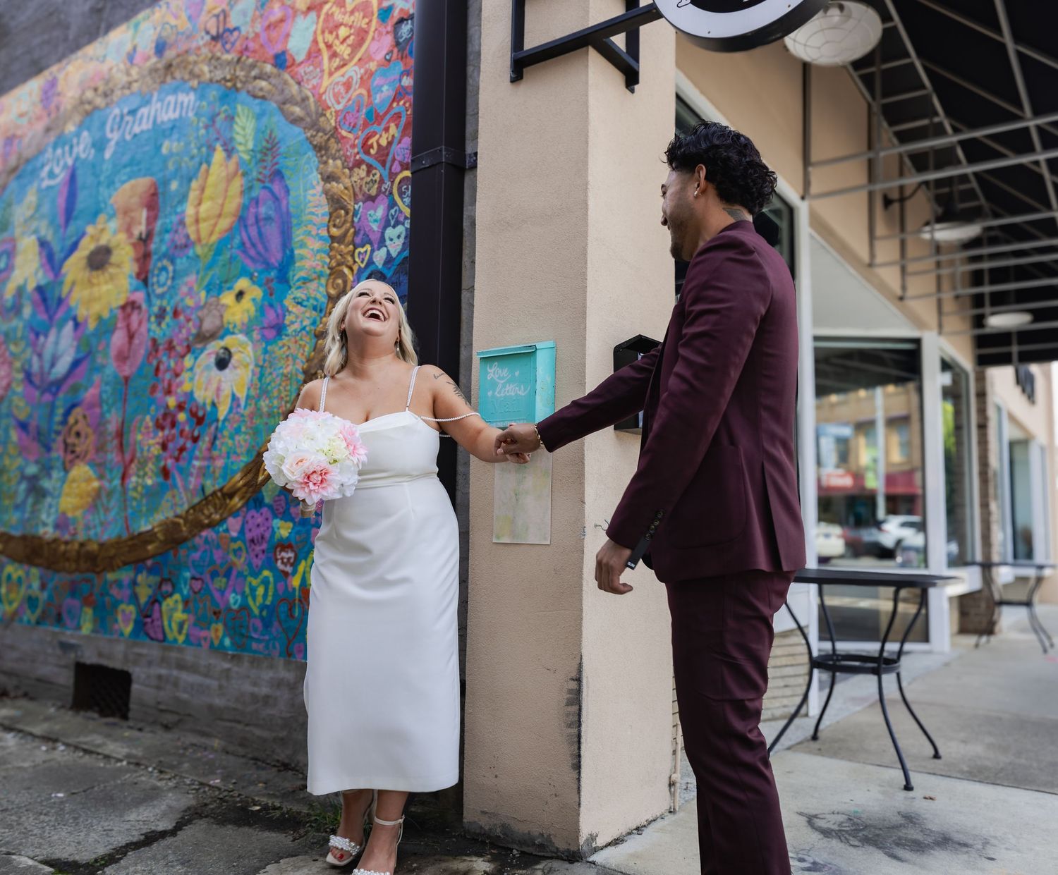 A couple sharing a playful moment in front of a bright floral mural.