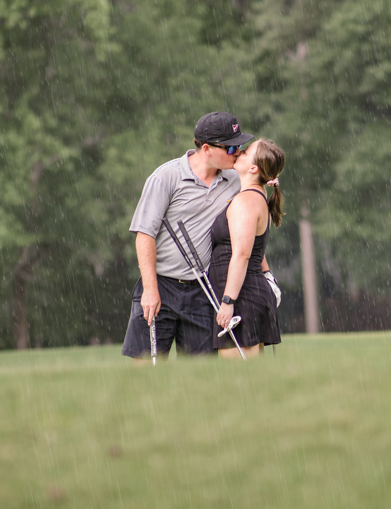 A couple shares a tender moment while walking together on a grassy hill in a park setting.