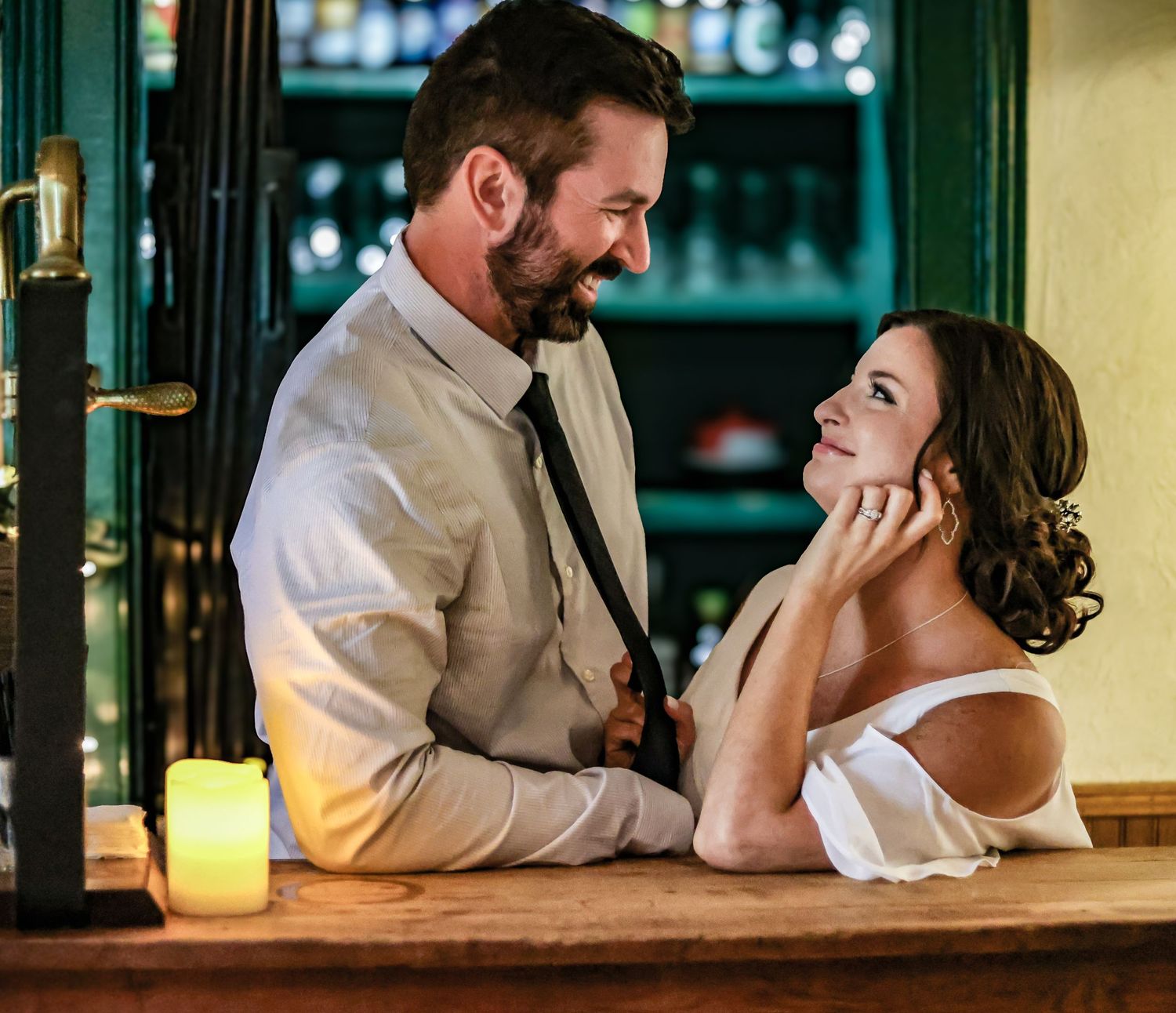 A romantic couple leans in close at a dimly lit bar counter sharing an intimate moment together.