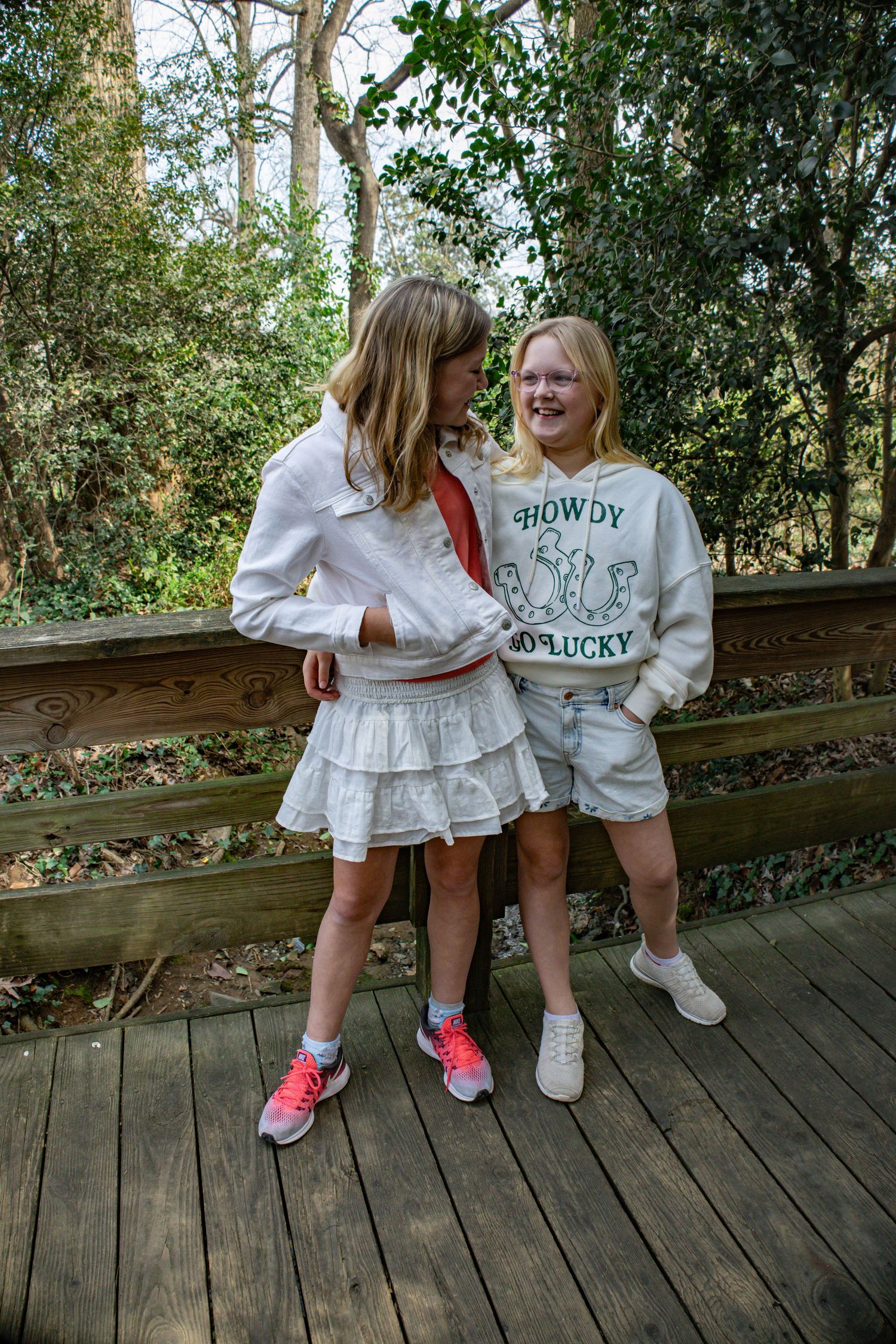Two people sharing a laugh on a wooden deck wearing casual sportswear and sneakers.