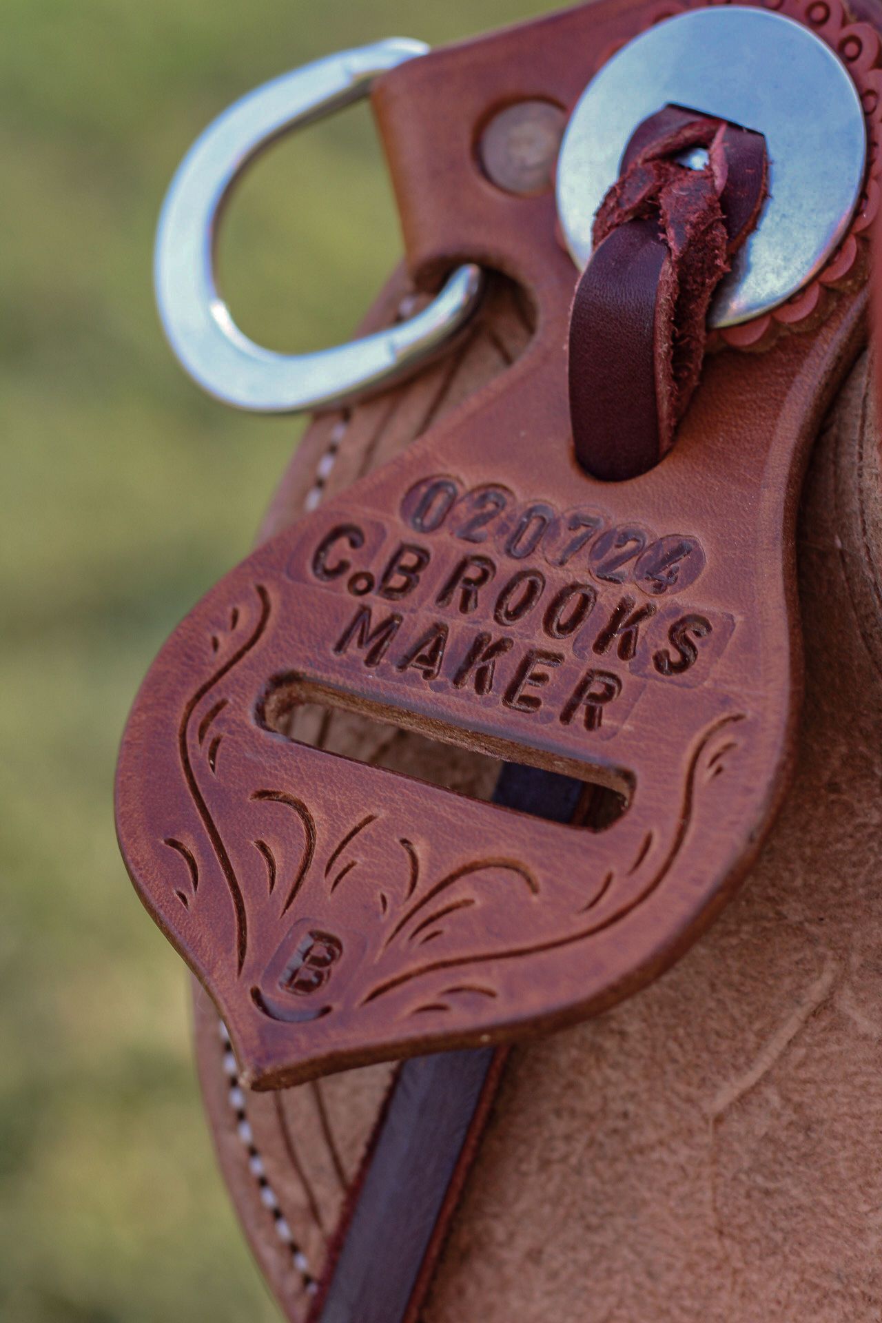 Close-up of a G.B Brooks Maker leather saddle tag with decorative scrollwork.