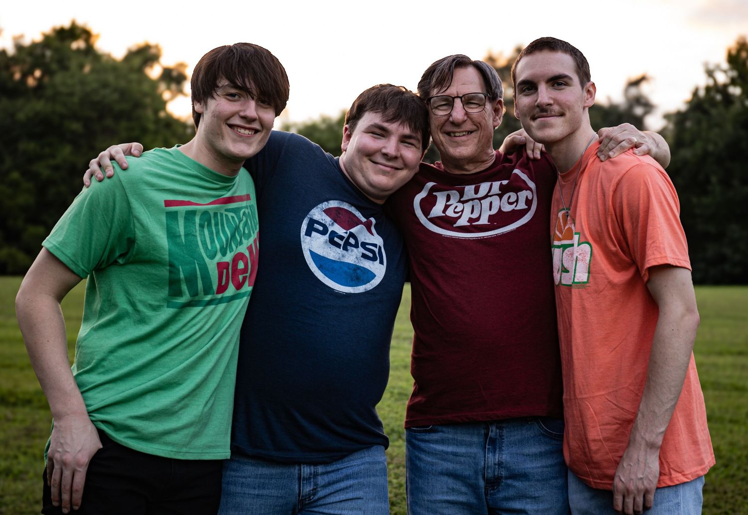 A group of friends wearing casual t-shirts pose together outdoors during golden hour.