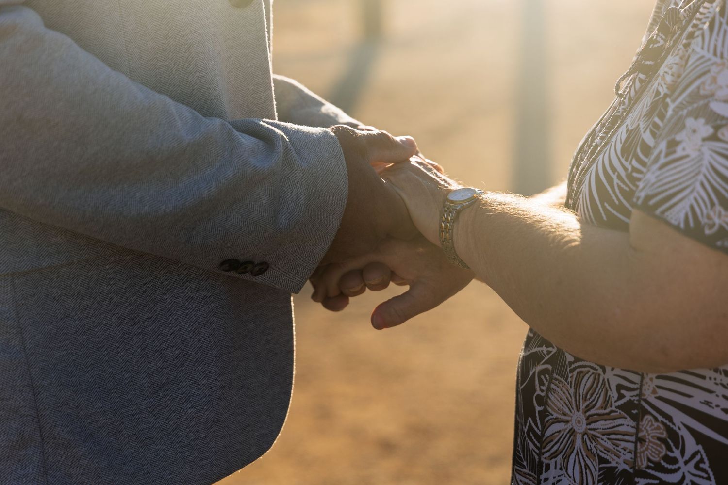 A close-up shot of two people's hands exchanging a cup of coffee in warm sunlight.