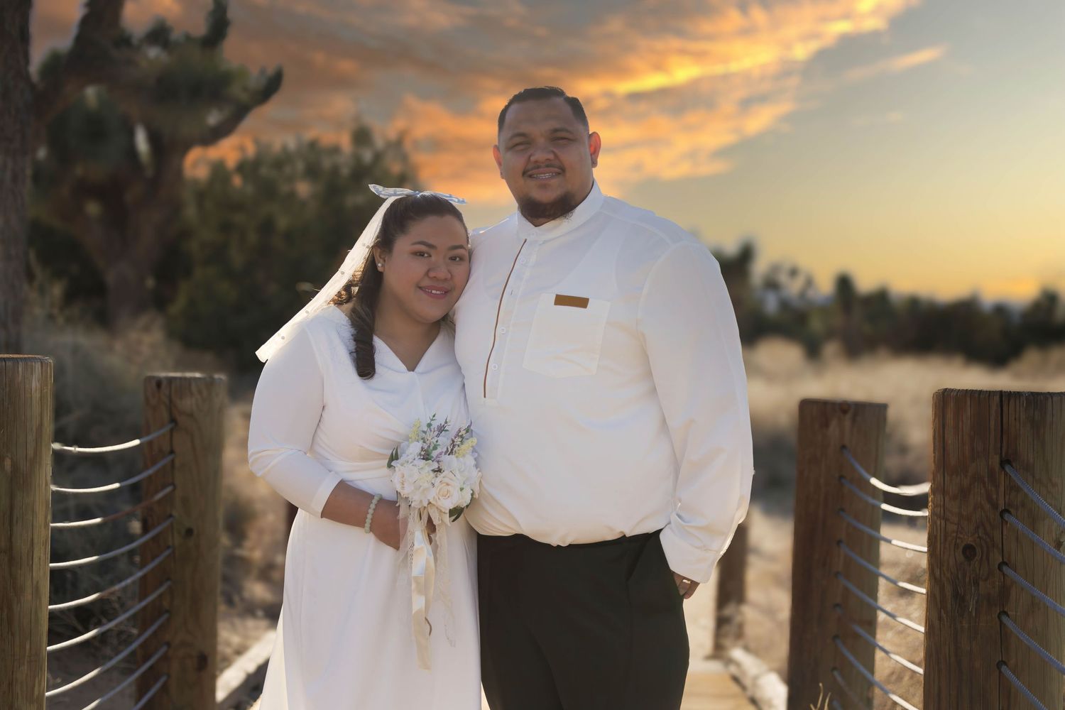 Newlyweds pose together at sunset against wooden fence background.