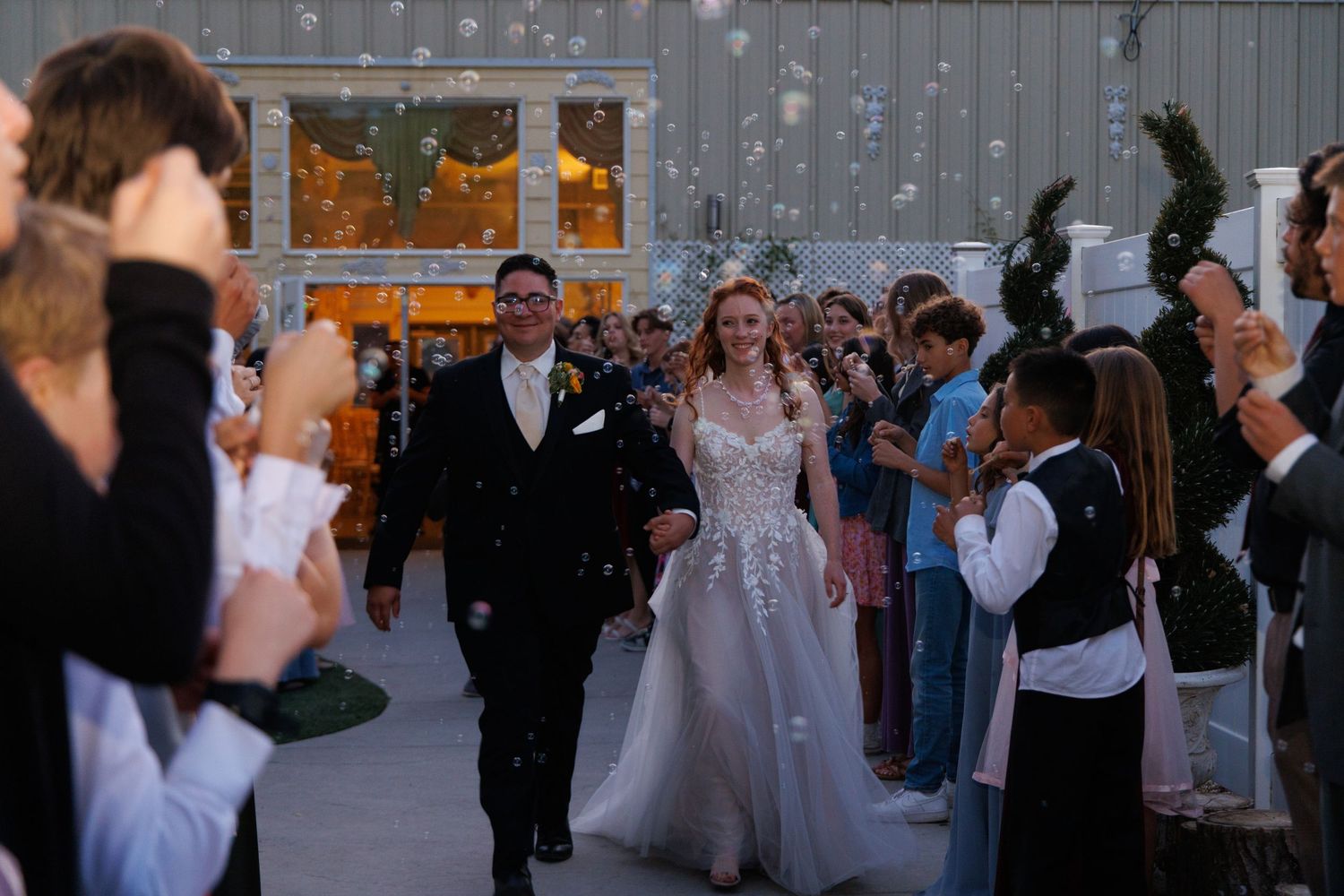 A couple exits their wedding ceremony as guests shower them with confetti at dusk.