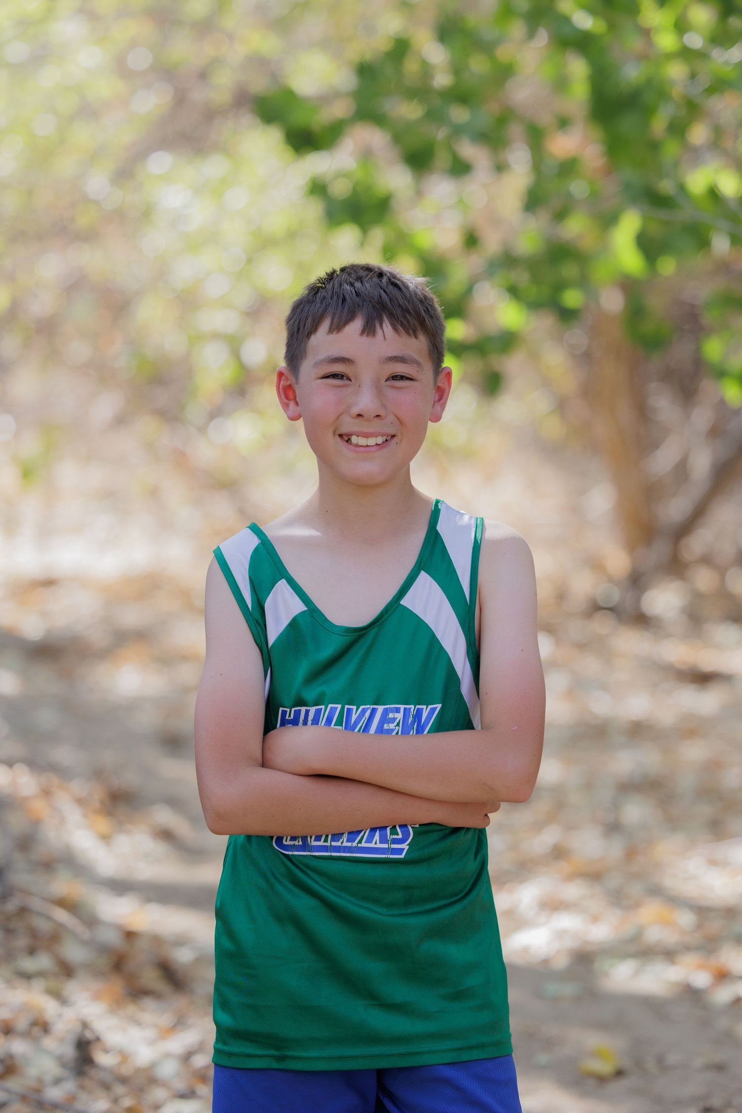 A young athlete poses in a green and white sports uniform outdoors.