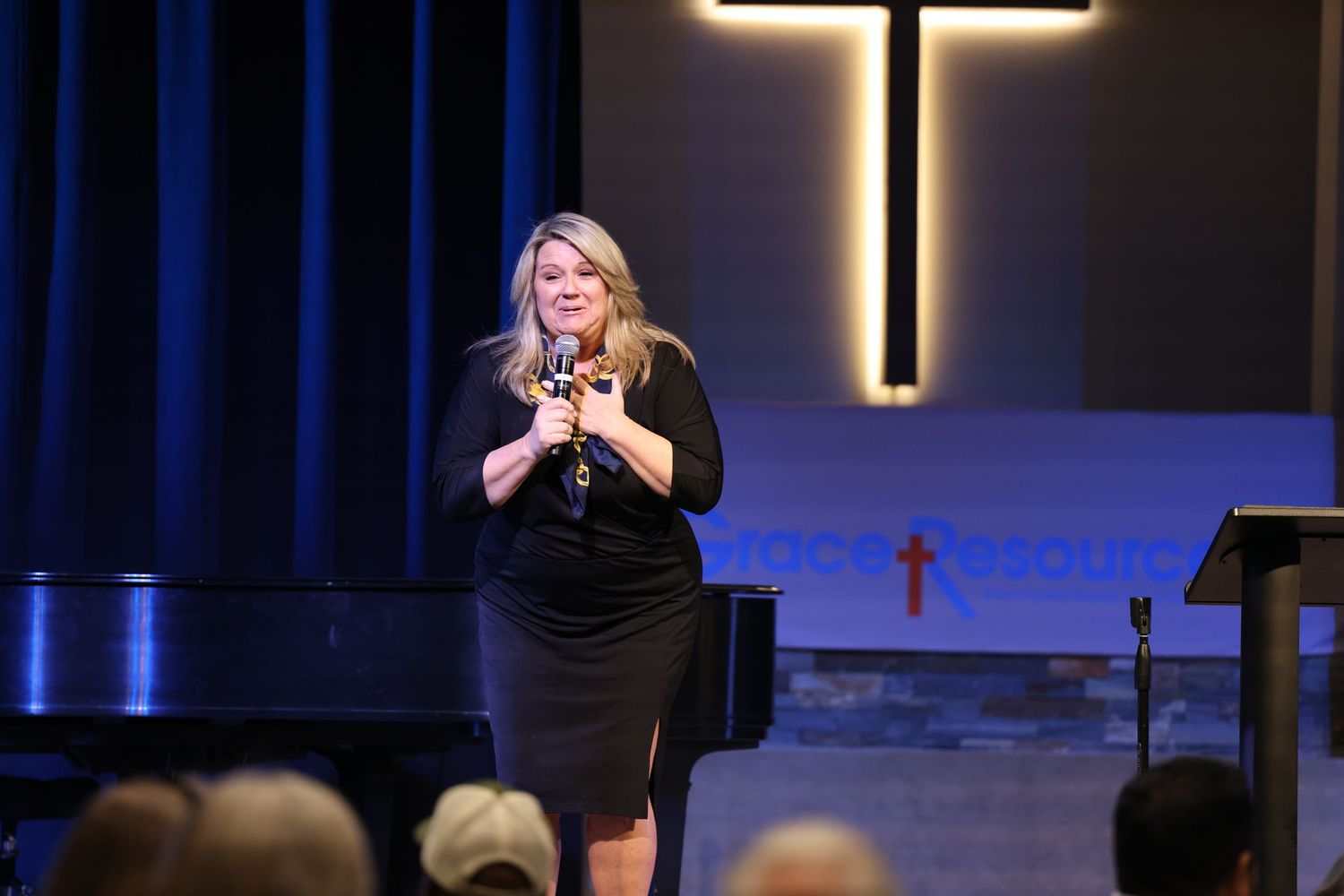 Woman performing onstage at church with illuminated cross in background.