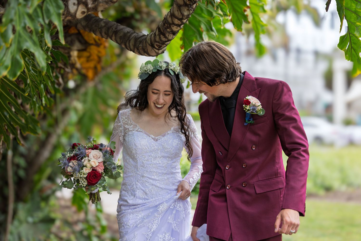 A joyful bride and groom share a candid moment outdoors, with the bride holding a burgundy floral bouquet.