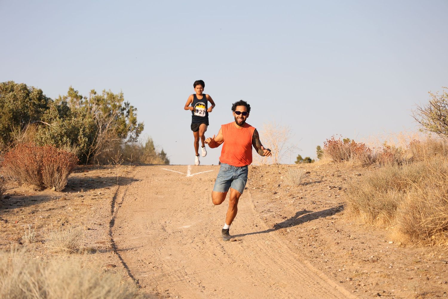Two people running together on a dirt trail through arid desert terrain.