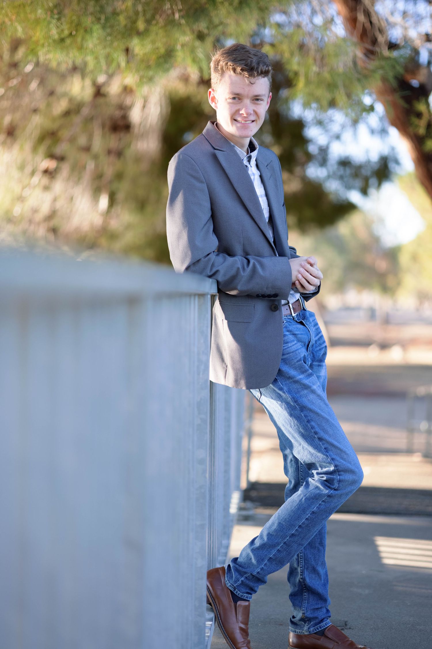 A casual portrait of someone leaning against a wall wearing a blazer and jeans outdoors.