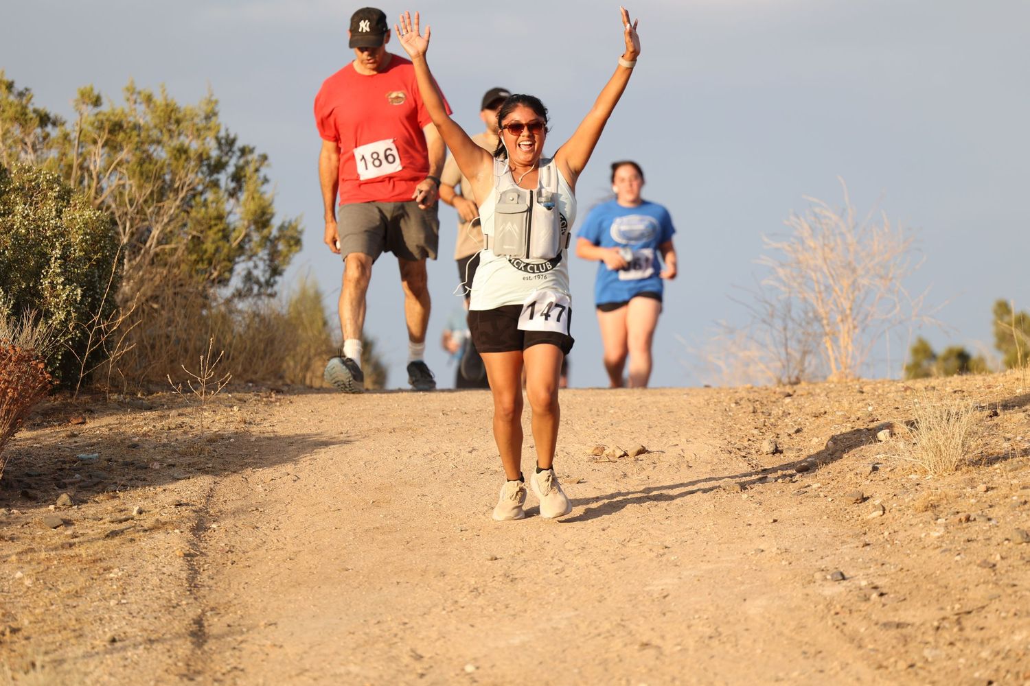 Trail runners celebrating and raising arms while running on a desert path.