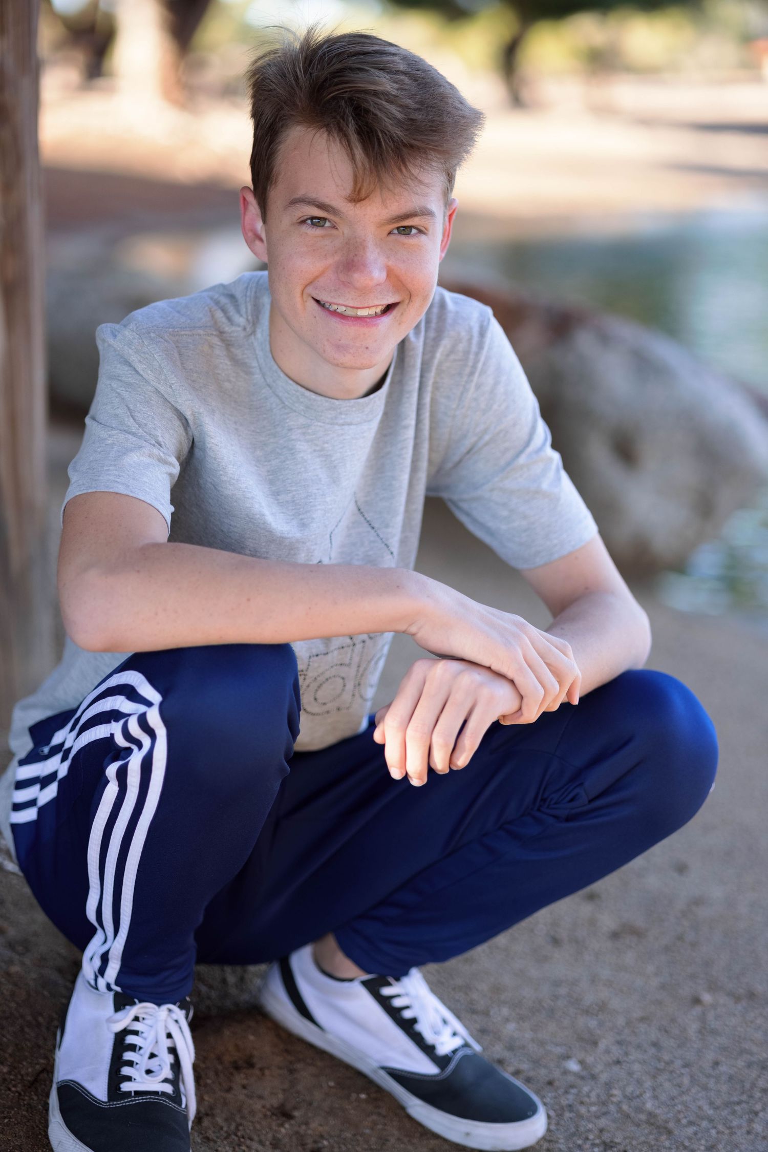 A casual outdoor portrait of someone in athletic wear crouching against a wall.