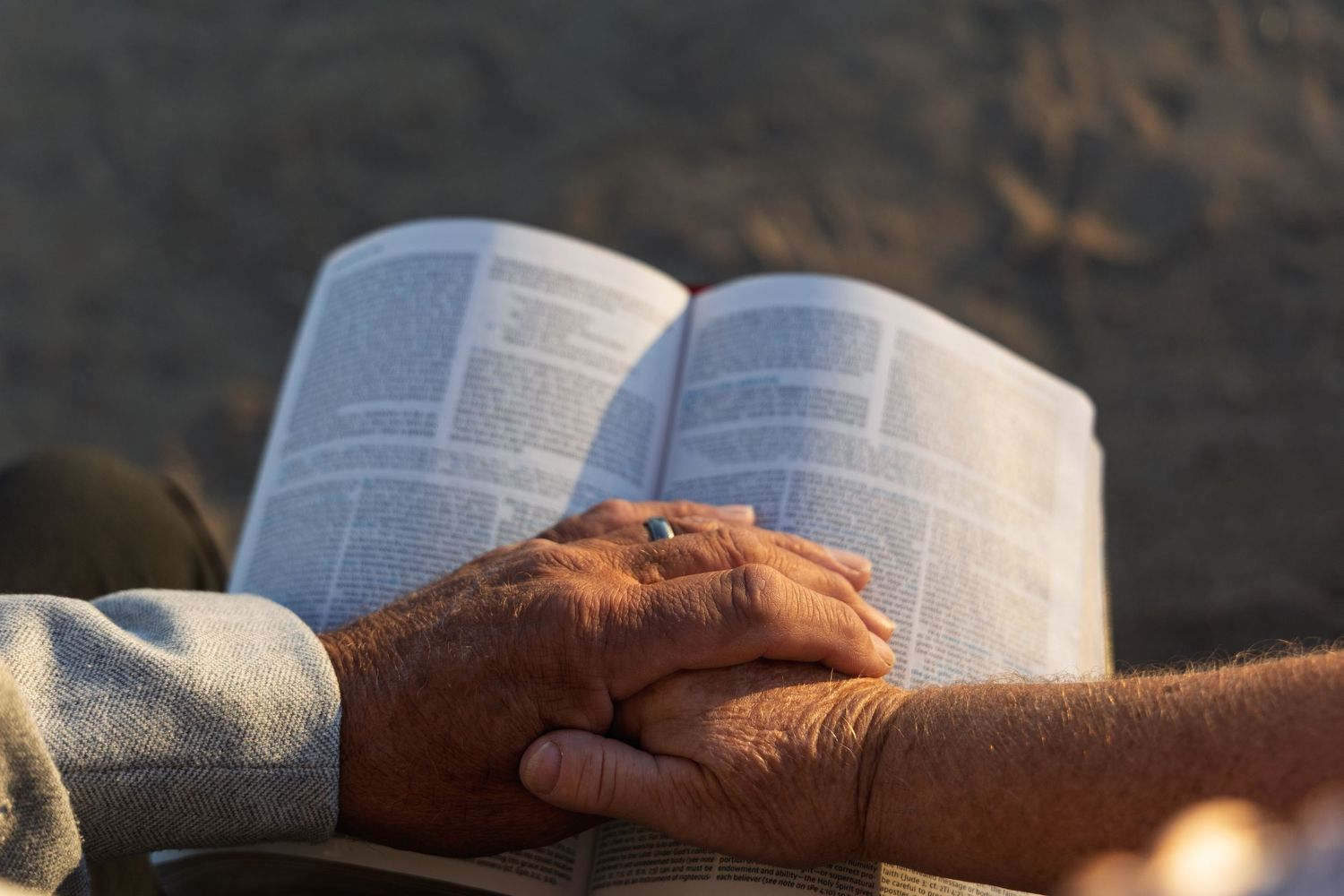 An open Bible rests on a stone surface with sunlight illuminating its pages in a serene outdoor setting.