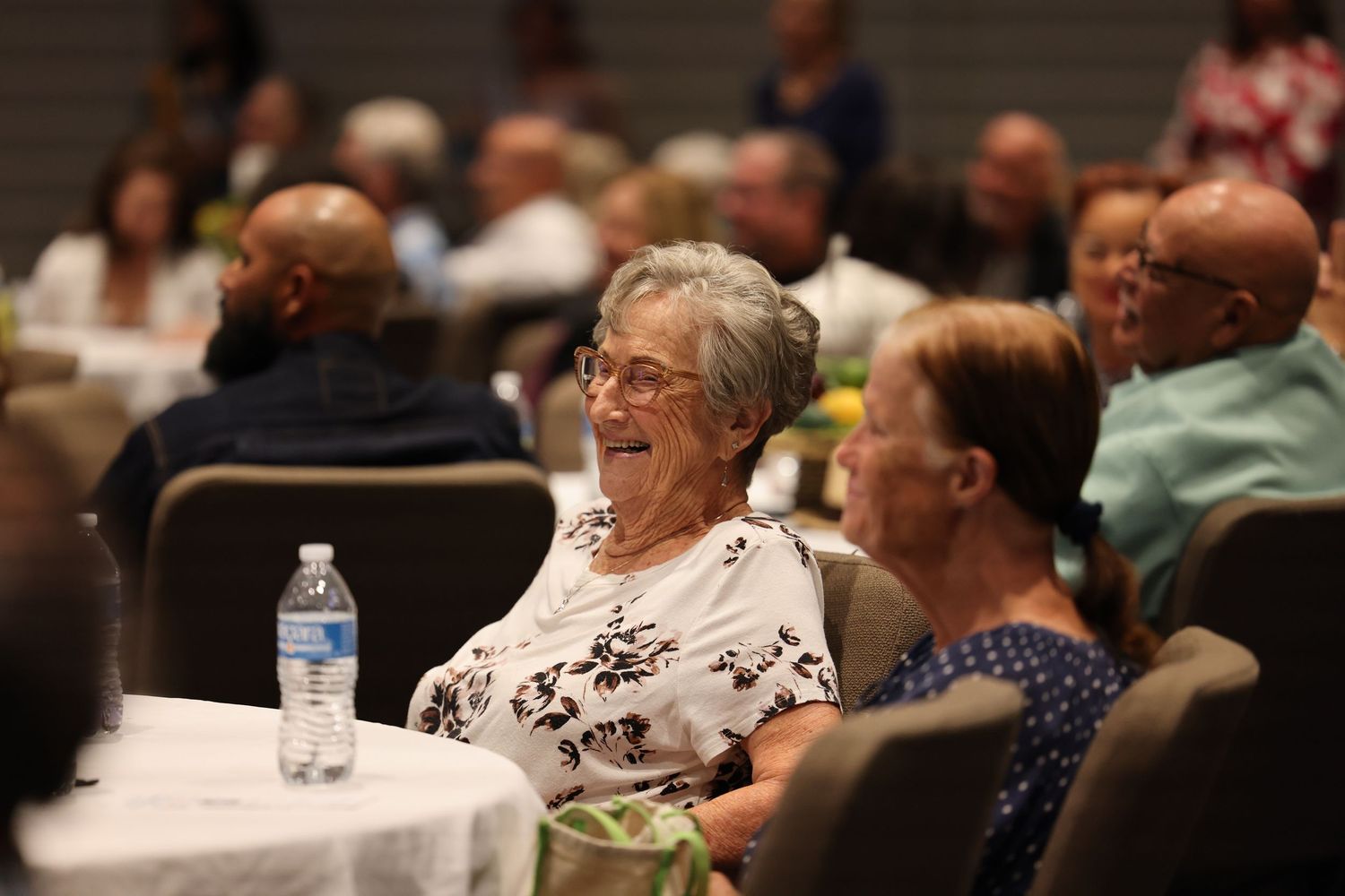 An audience member laughs during an indoor event seated at a round table.