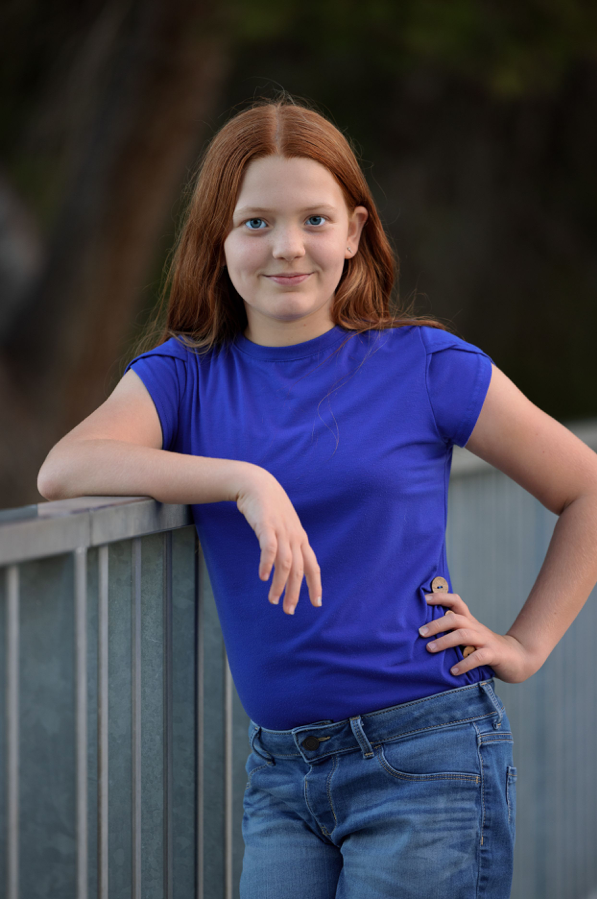 Young person in blue t-shirt posing casually against railing outdoors.