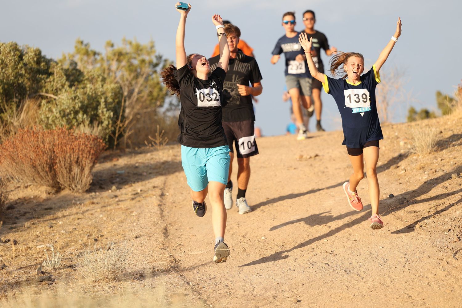Excited runners celebrating with raised arms while running on dirt trail during race.