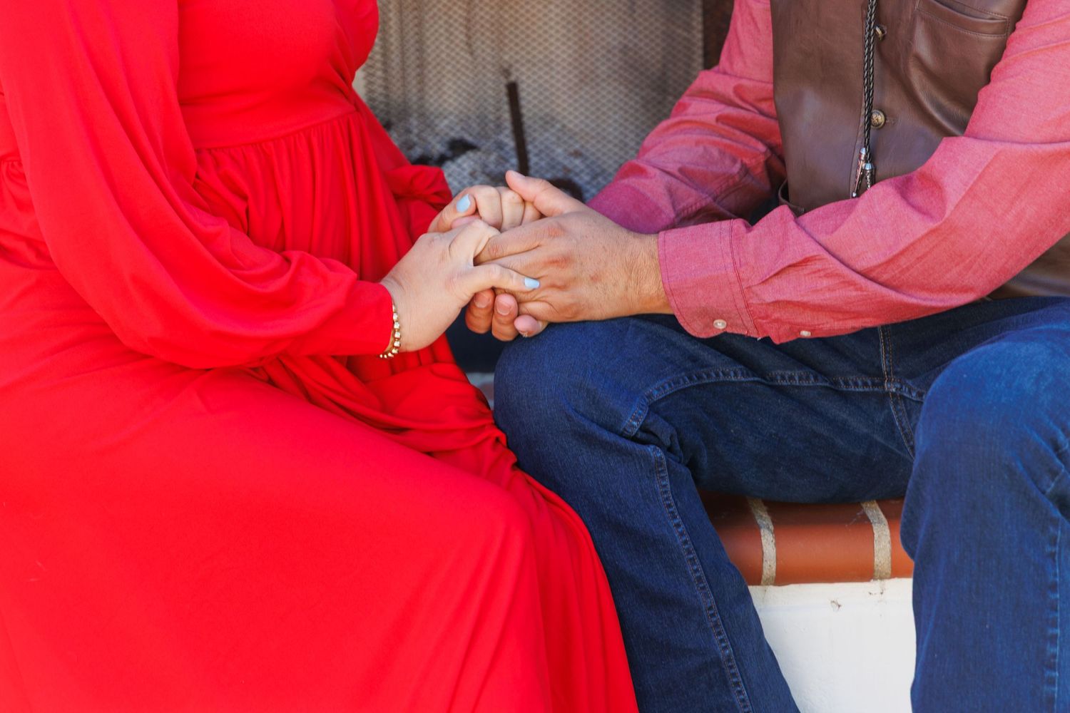 Two people holding hands while sitting together, one wearing a vibrant red dress.