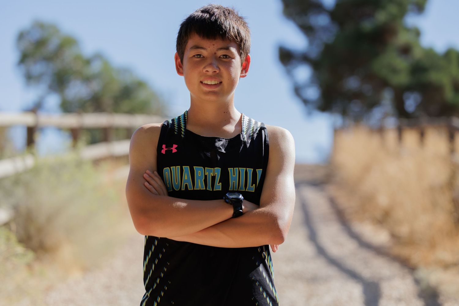 An athlete poses confidently in a dark athletic uniform on a dirt path.